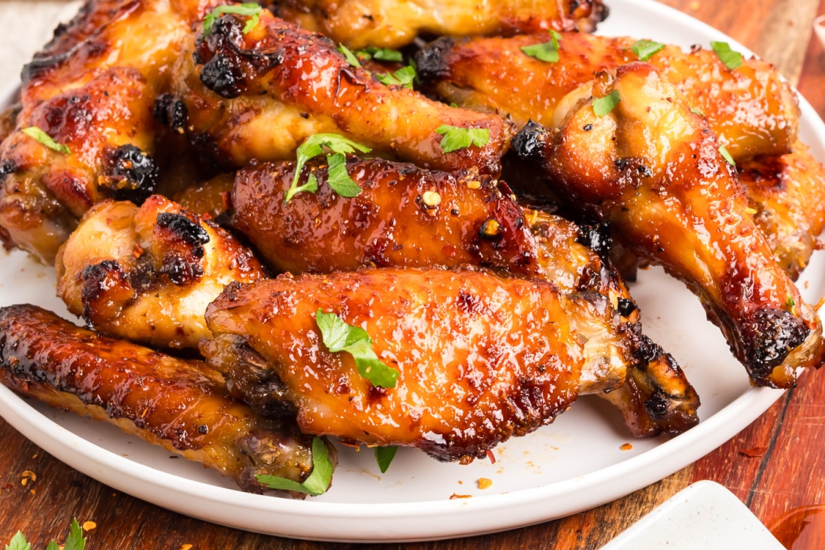 Oven baked honey garlic wings with parsley garnish. Oven baked honey garlic wings served on a white plate, saucy and crisp.