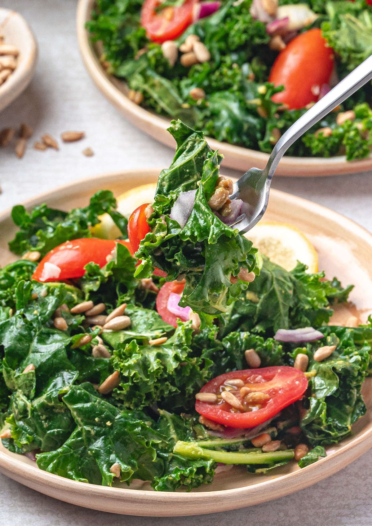 Forkful of avocado kale salad with cherry tomatoes, sunflower seeds, and red onion showing the creamy lemon dressing and fresh texture.