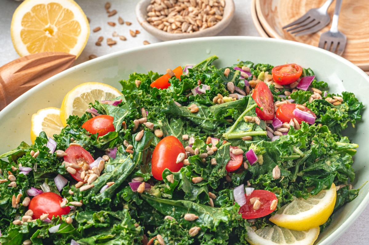 Creamy avocado kale salad with lemon dressing, cherry tomatoes, sunflower seeds, and red onion in a serving bowl.