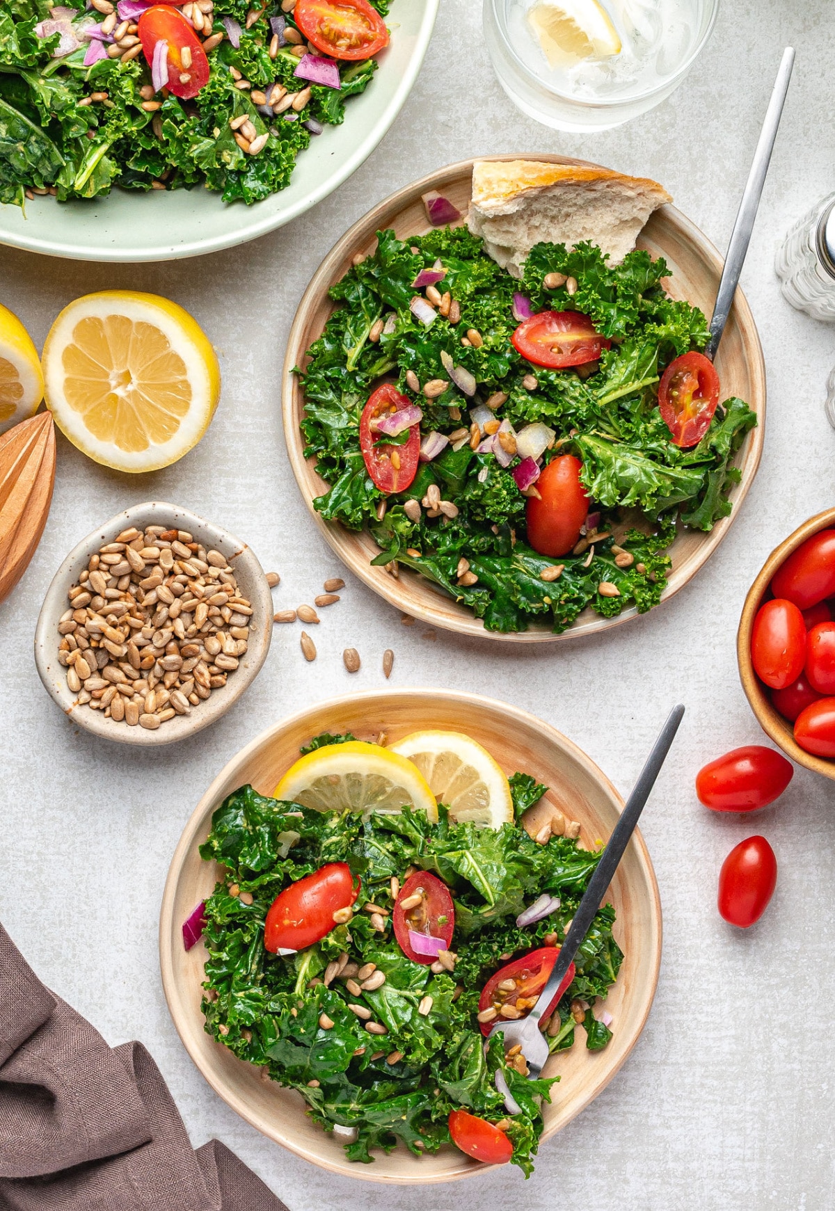 Avocado kale salad served on plates with lemon slices, sunflower seeds, and cherry tomatoes for a fresh cool-season meal.