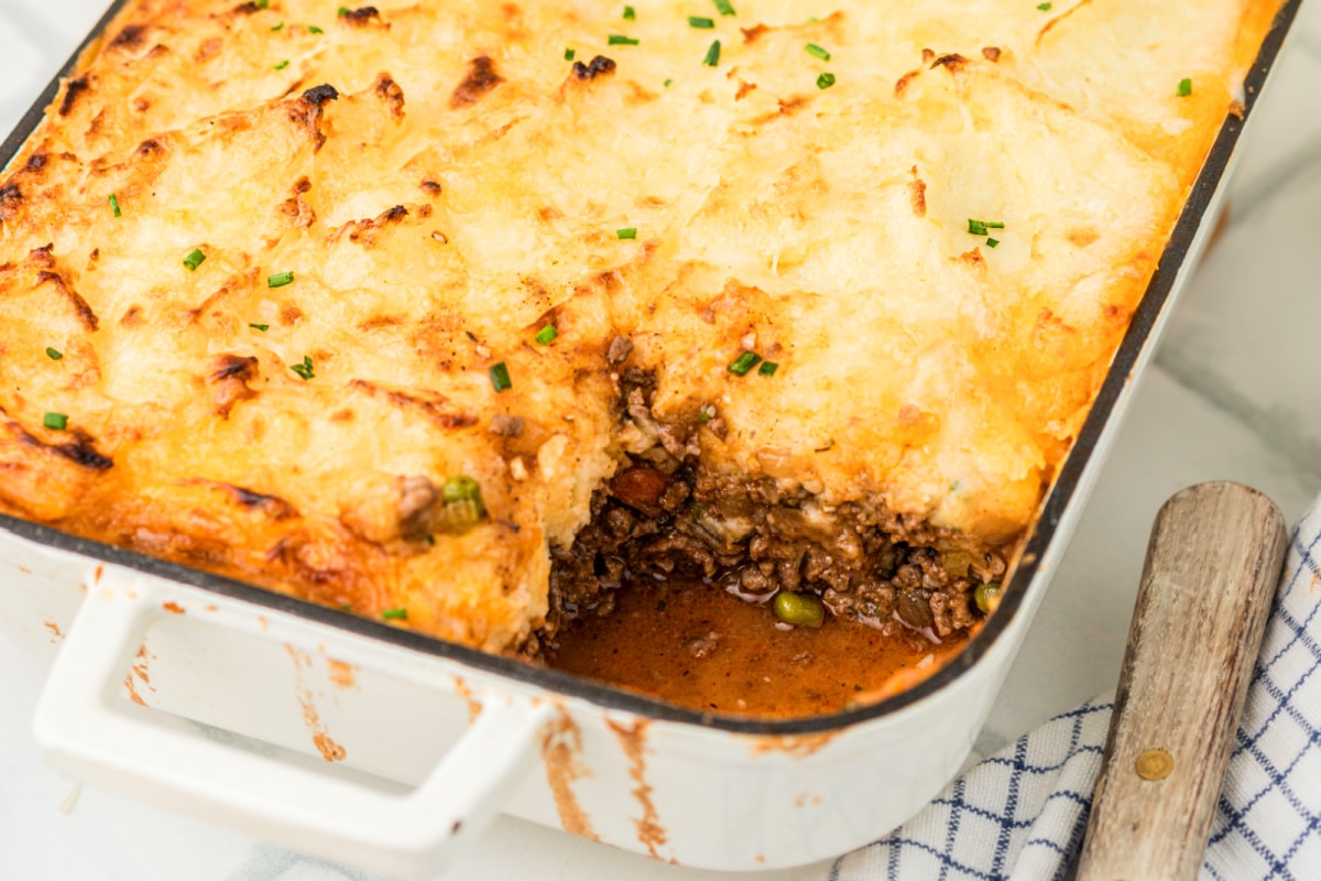 cottage pie with gruyere mashed potatoes in baking dish Cottage pie with Gruyère mashed potatoes in a white baking dish with a serving removed, showing the browned beef filling beneath the golden mashed topping.
