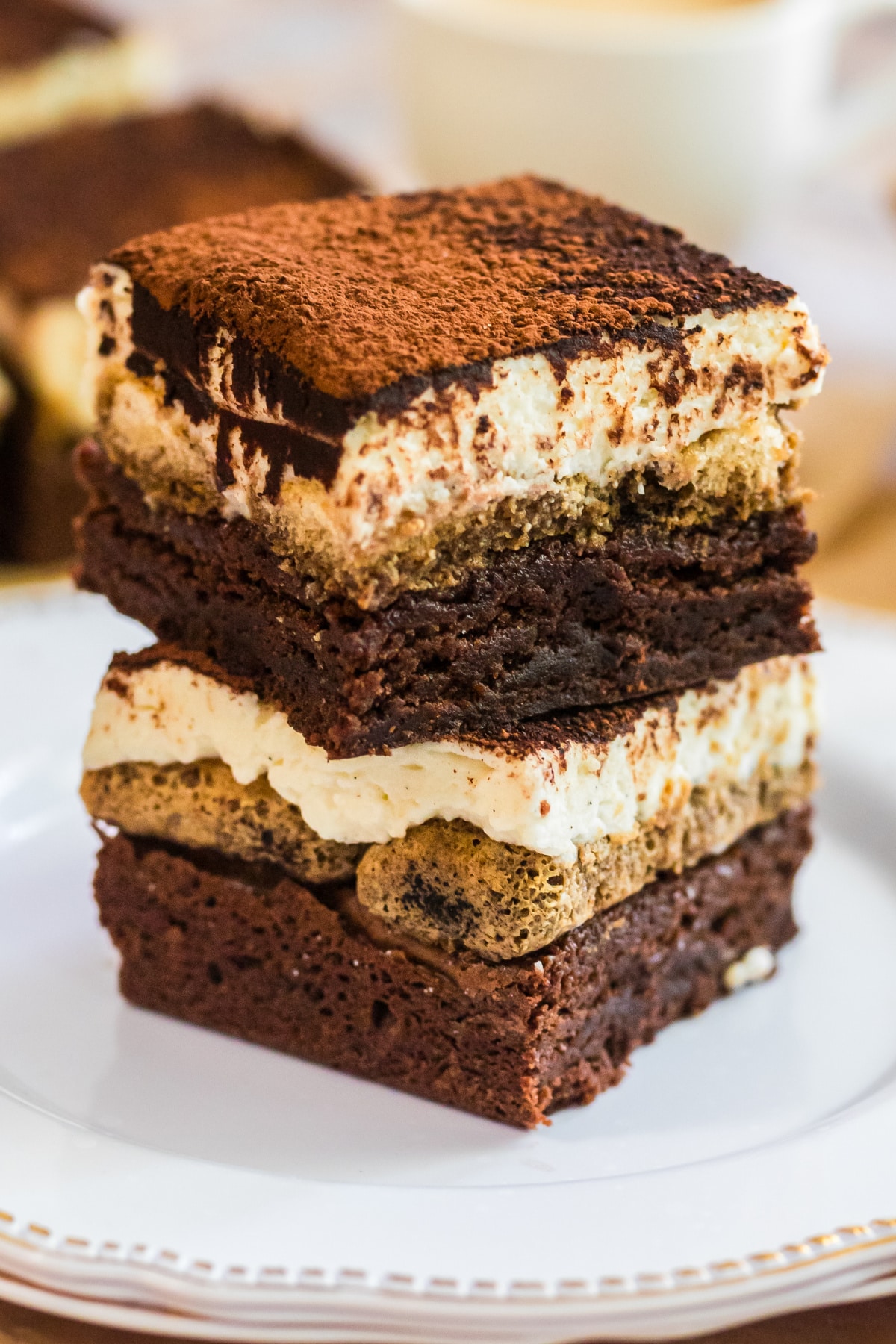 tiramisu brownies stacked on a plate showing espresso-soaked layers, mascarpone cream, and cocoa powder topping.