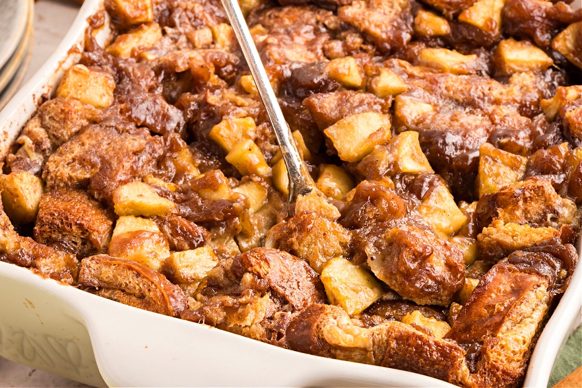 Freshly baked caramel apple bread pudding in a white dish with chunks of brioche and tender apples in caramel sauce. 