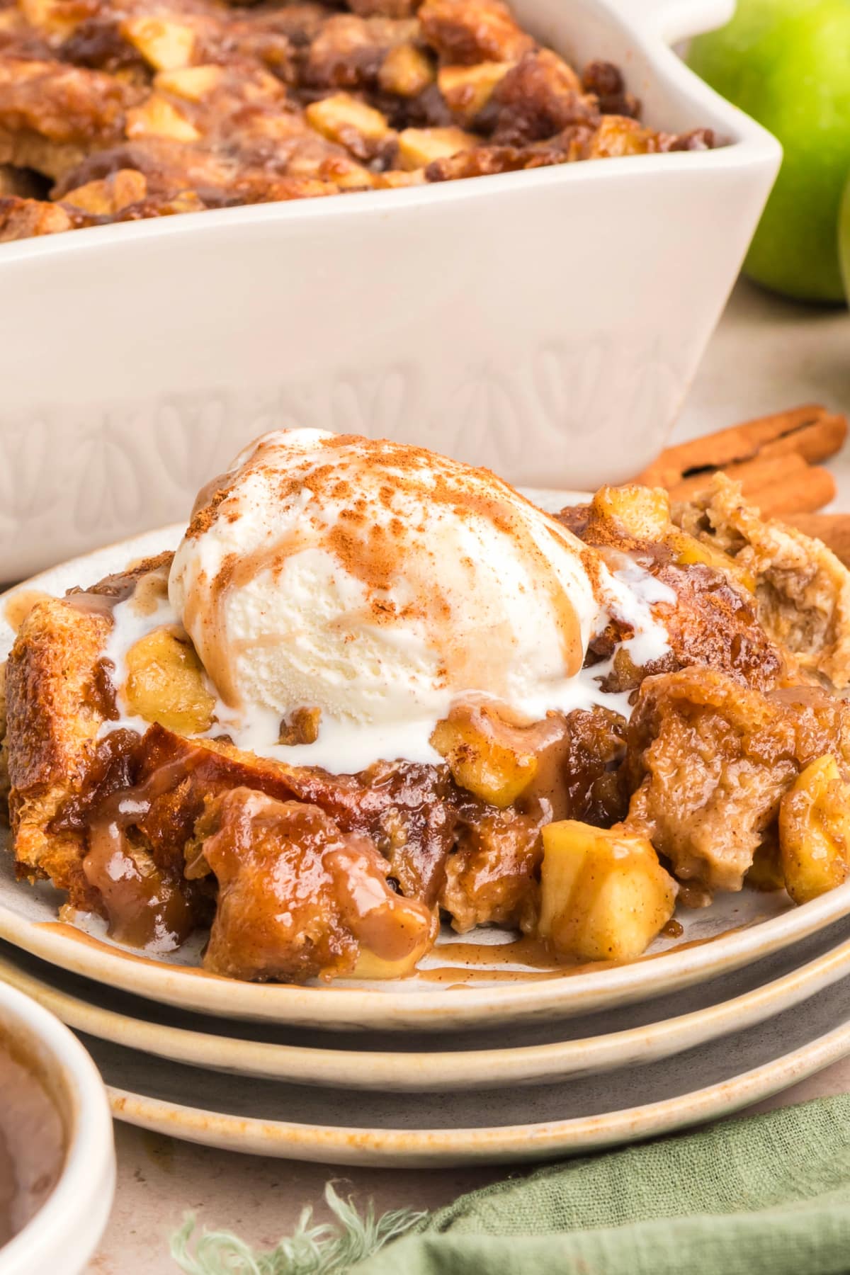 Close-up of custardy brioche bread pudding with caramel sauce and soft baked apples topped with melting vanilla ice cream. 