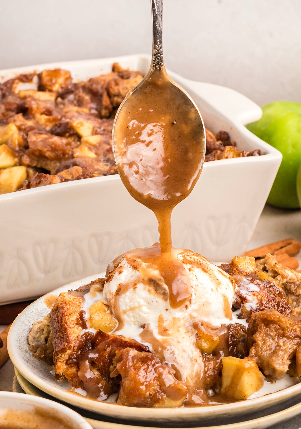 Spoon drizzling caramel sauce over warm bread pudding topped with vanilla ice cream, showing the rich texture and glossy finish.