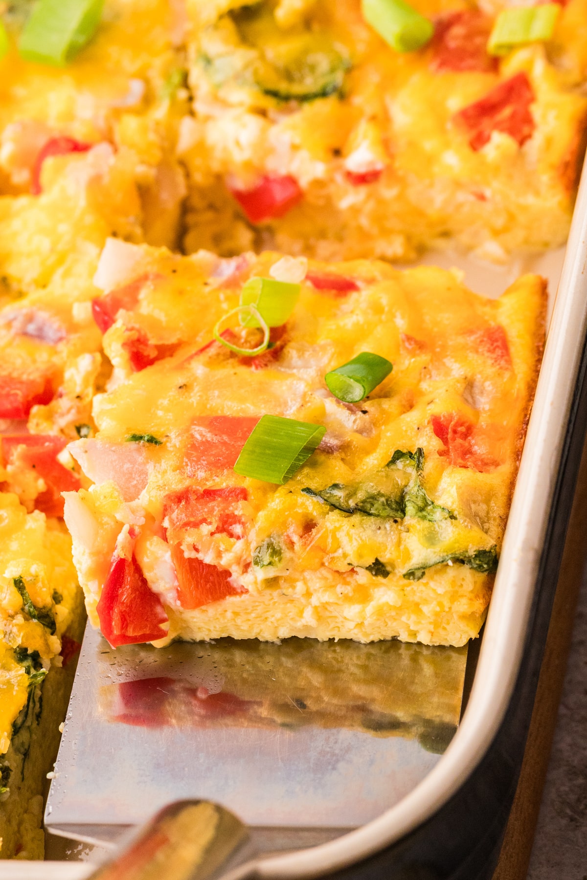 Close view of cheesy egg bake square High protein cottage cheese egg bake with cheddar, peppers, and spinach on spatula