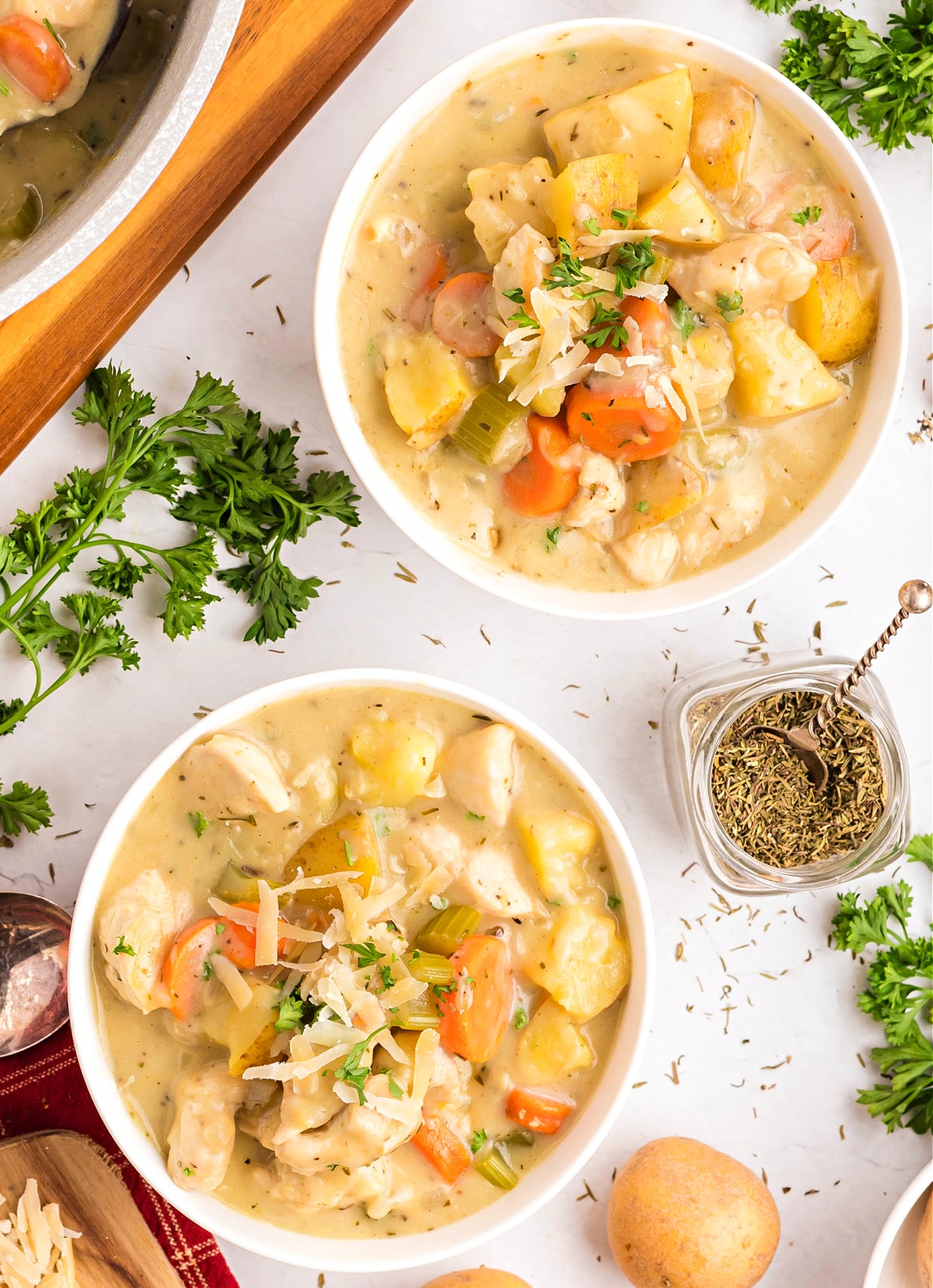 creamy chicken stew in bowls creamy chicken stew in white bowls with potatoes, carrots, and celery in a rich broth, topped with parsley and Parmesan.