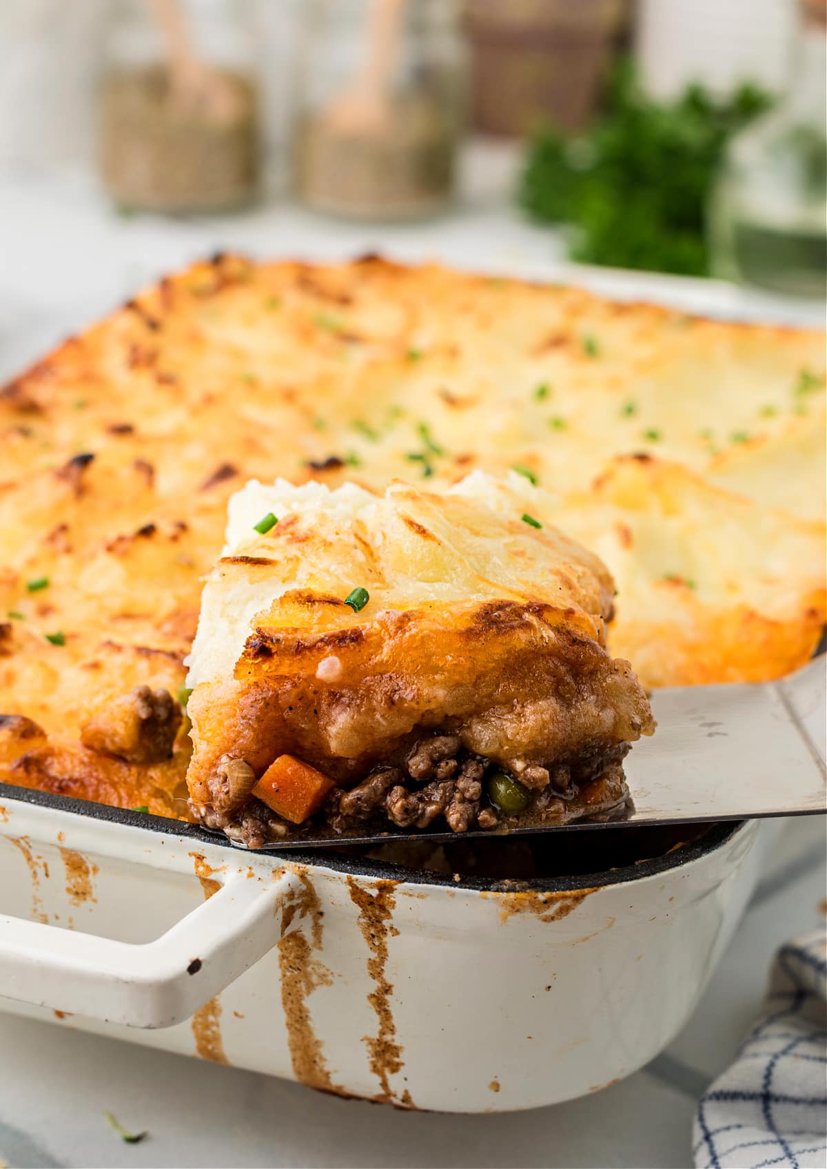 cottage pie slice lifted from pan Cottage pie with Gruyère mashed potatoes being lifted from a baking dish, showing browned beef, peas, and carrots under a golden mashed potato topping.