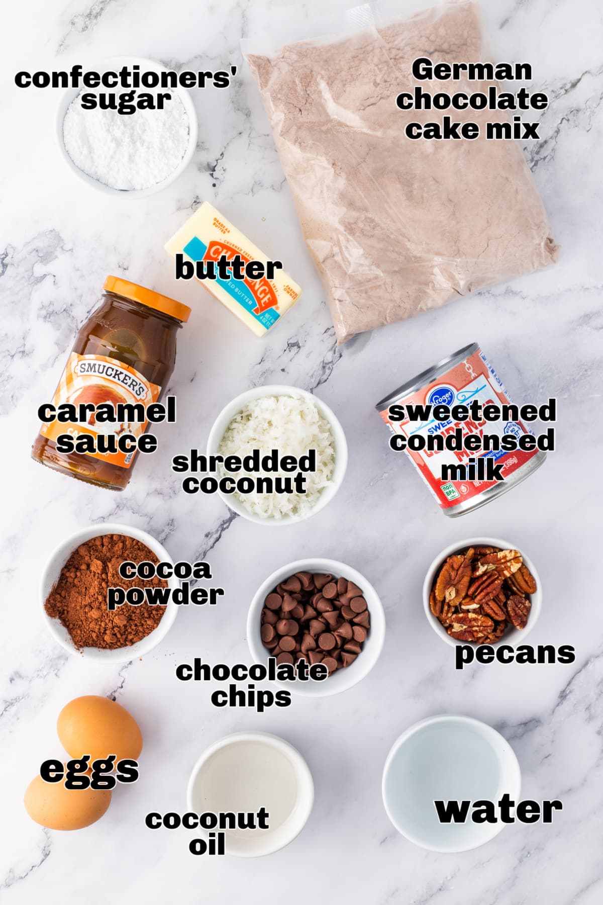 Ingredients for German chocolate poke cake on marble surface Overhead view of labeled ingredients for making German chocolate poke cake including cake mix, coconut oil, caramel sauce, and sweetened condensed milk.