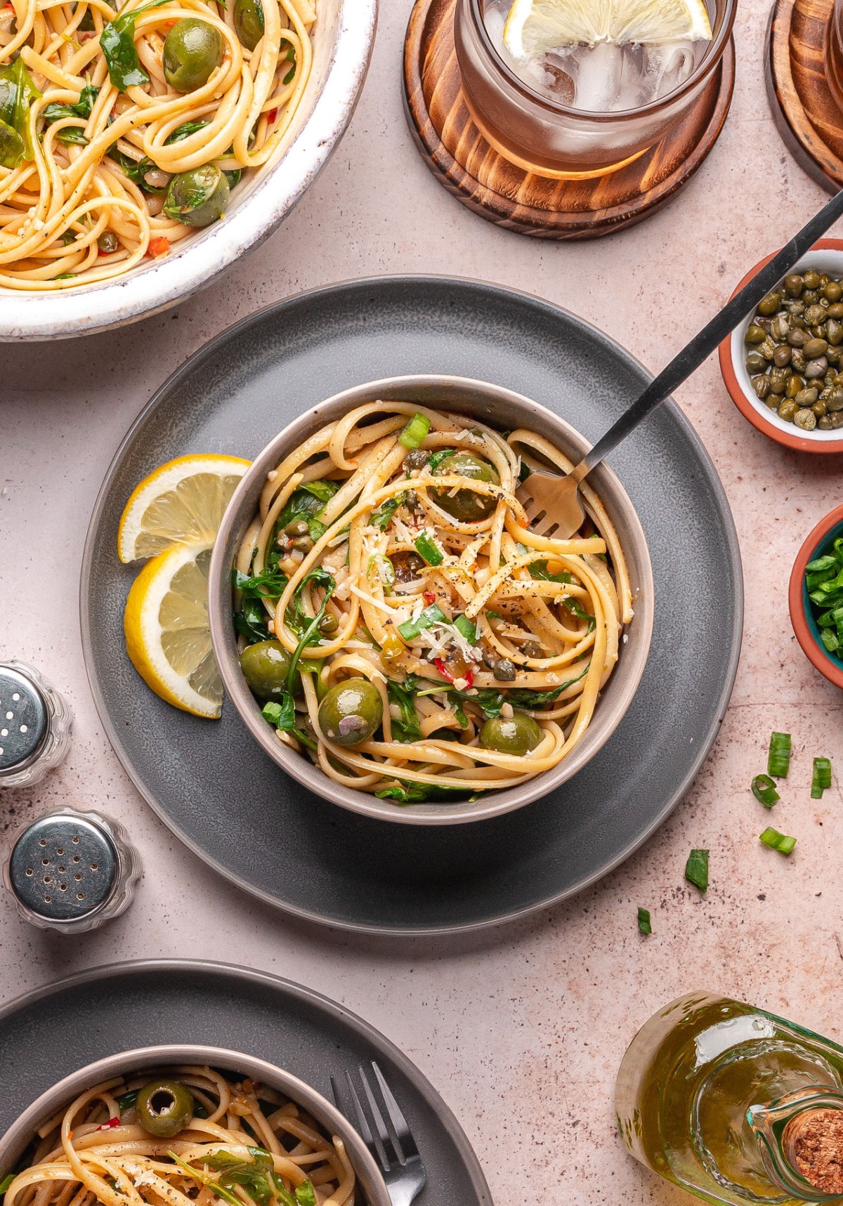italian-pasta-with-olives-served-with-lemon Italian pasta with olives served in gray bowls with lemon slices and grated Parmesan.