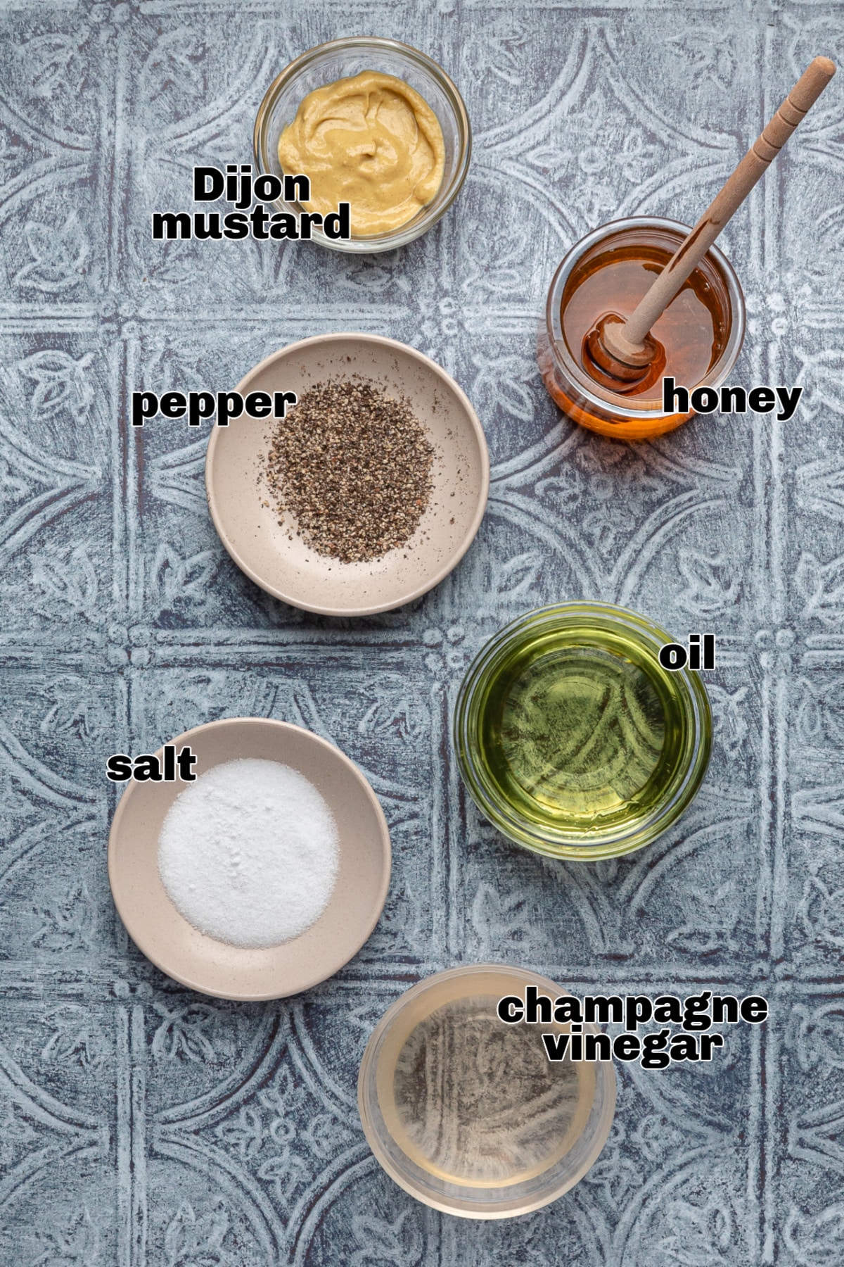 Honey Champagne Vinaigrette Ingredients Flat Lay Ingredients for honey champagne vinaigrette on a blue surface, including Dijon mustard, honey, oil, champagne vinegar, salt, and pepper.