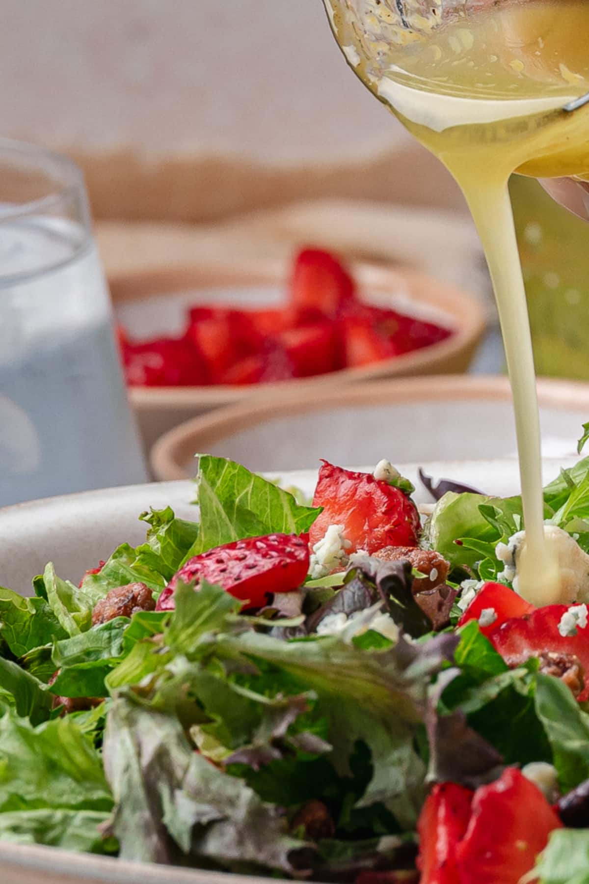 Pouring Dressing Over Strawberry Salad Pouring homemade salad dressing over a bowl of mixed greens with strawberries and cheese.