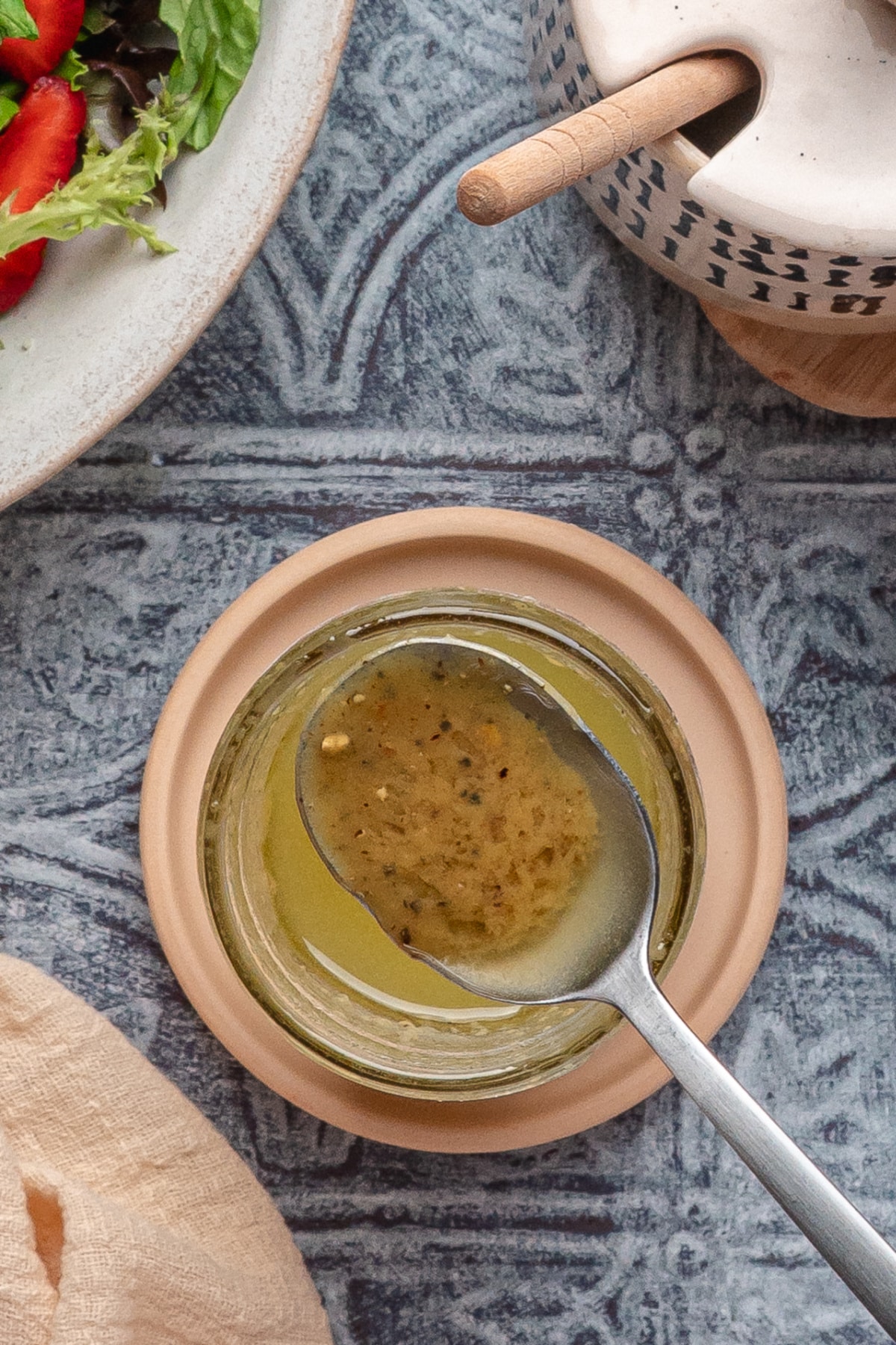 Spoonful of Dijon Honey Dressing Spoonful of homemade Dijon and honey dressing lifted from a glass jar on a textured blue surface.