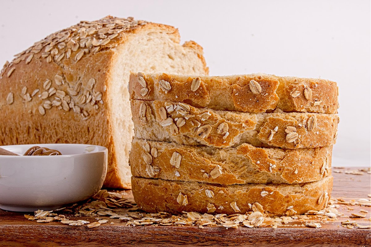 sliced honey oatmeal bread Sliced homemade honey oatmeal bread stacked on a board beside a bowl of honey.