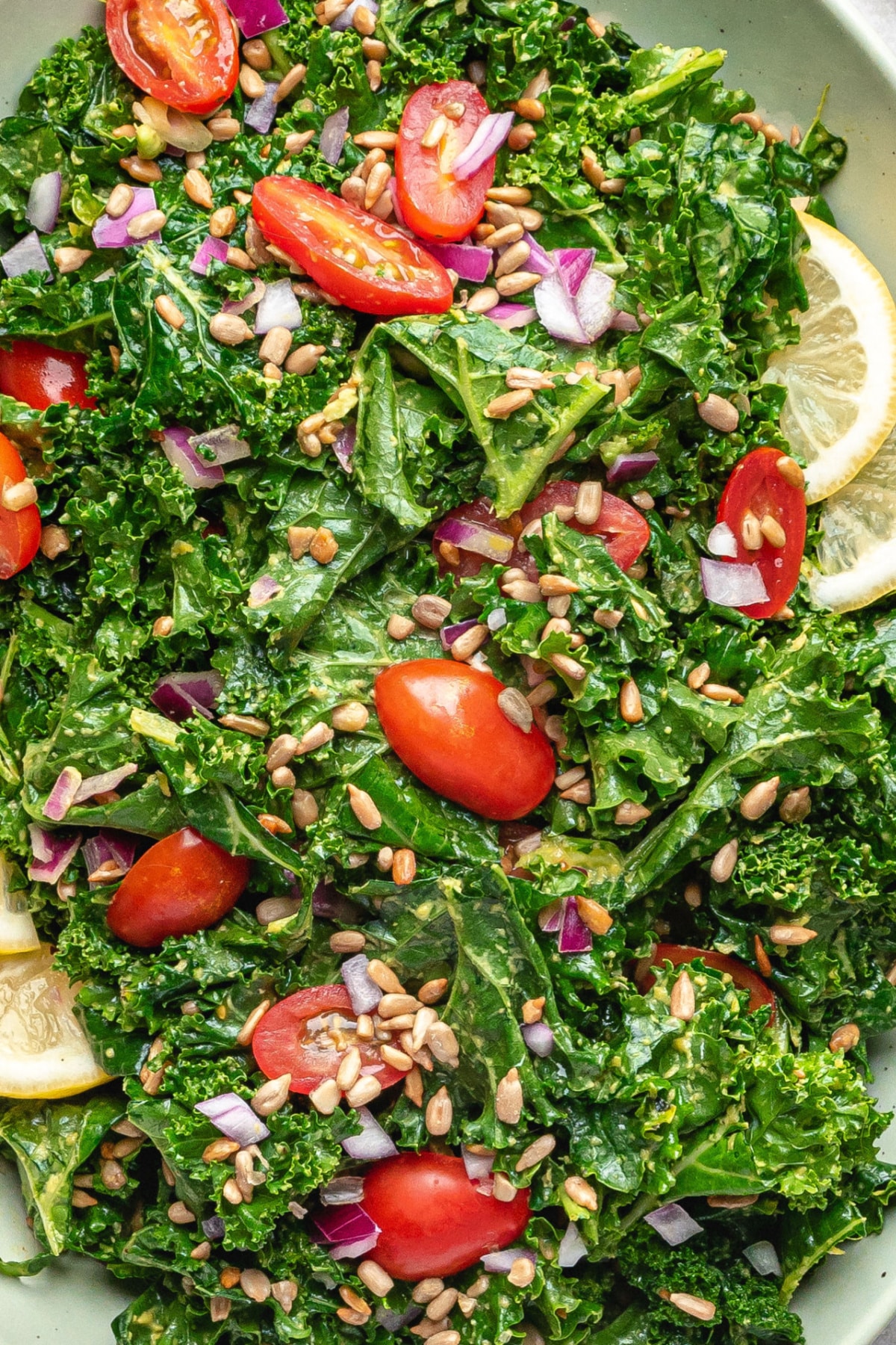 Close-up of avocado kale salad with lemon, sunflower seeds, red onion, and cherry tomatoes showing creamy texture and “cheesy” coating.