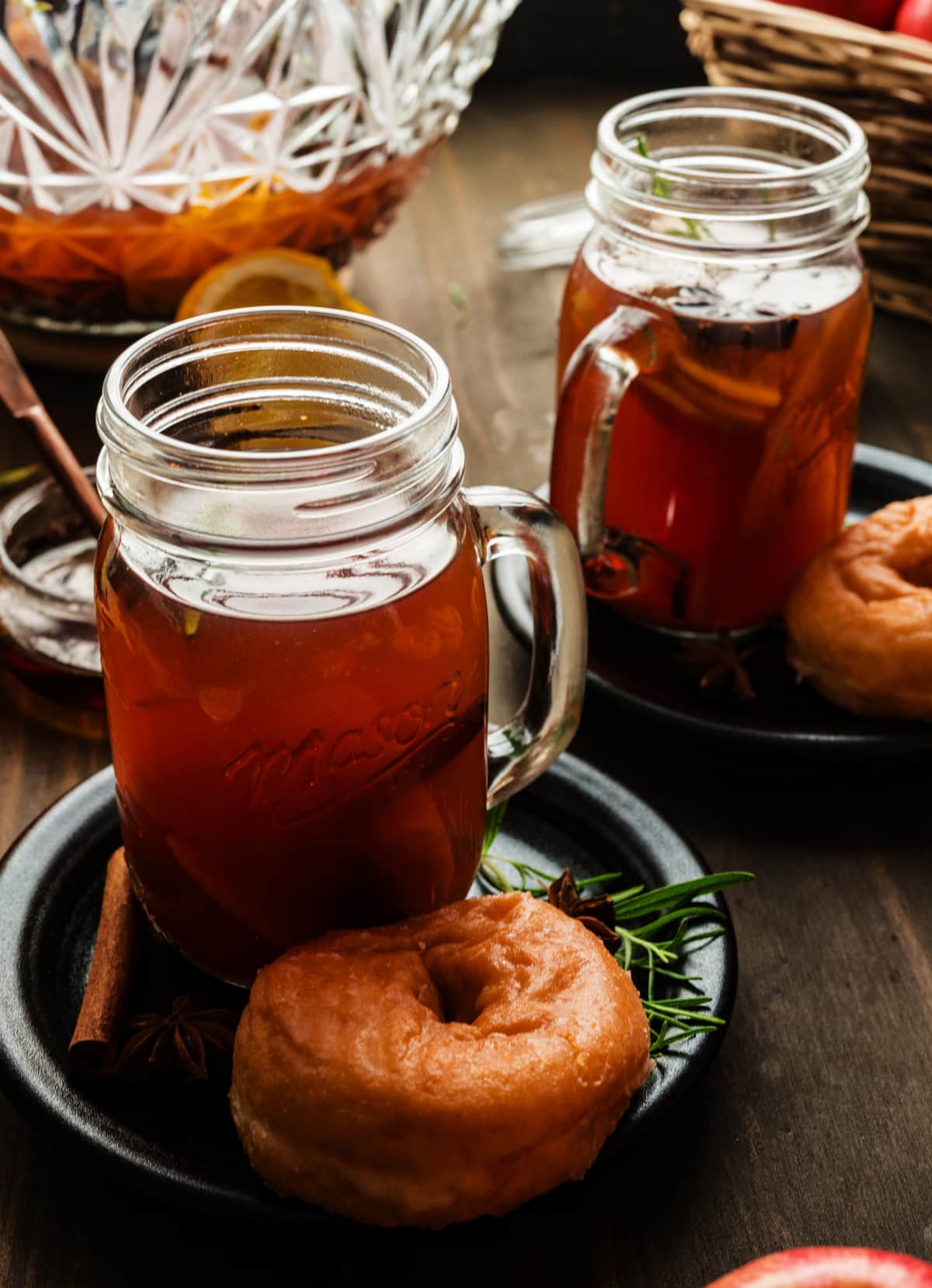 Two mugs of warm mulled cider served with glazed donuts, cinnamon sticks, and star anise, creating a fall dessert pairing.