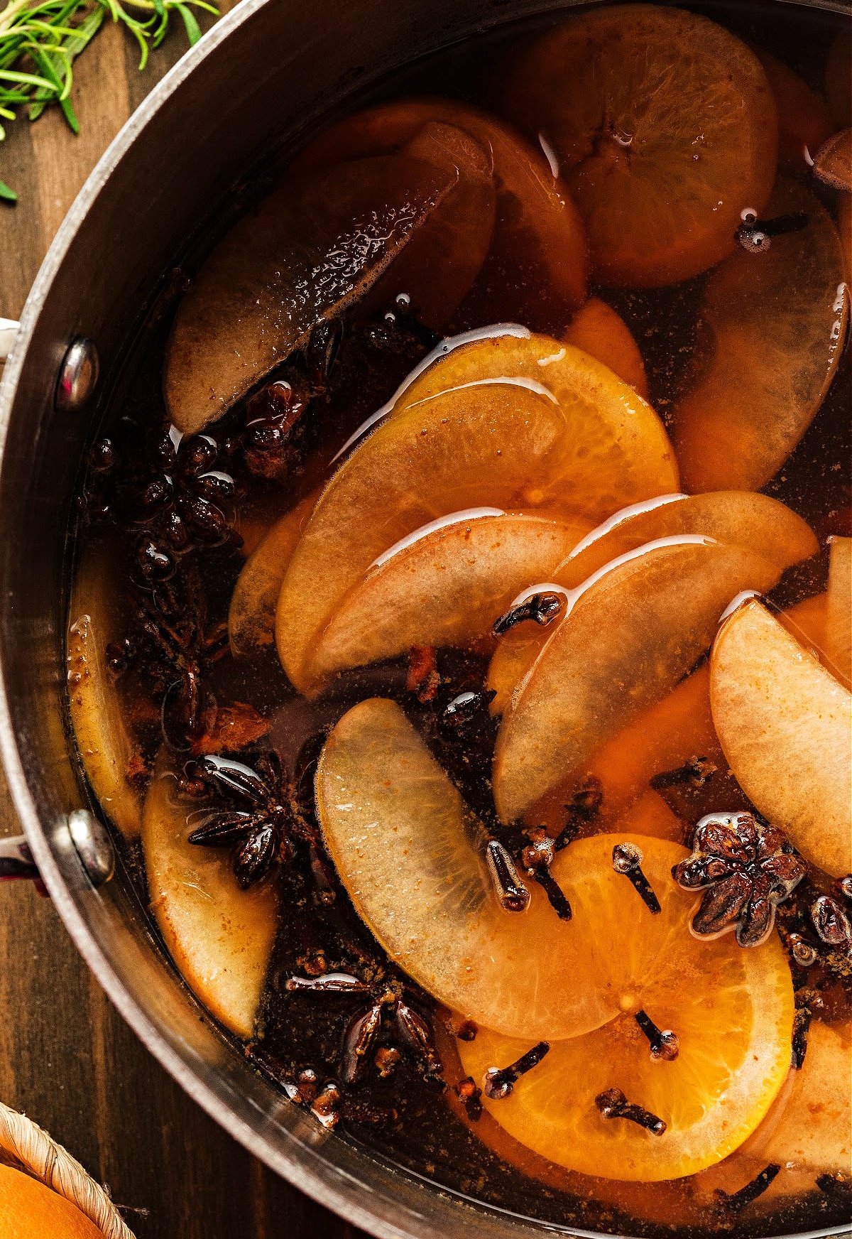 Apple and orange slices simmering in mulled cider with cloves, cinnamon sticks, and star anise floating in a deep amber liquid. Photographed for Noble Pig.