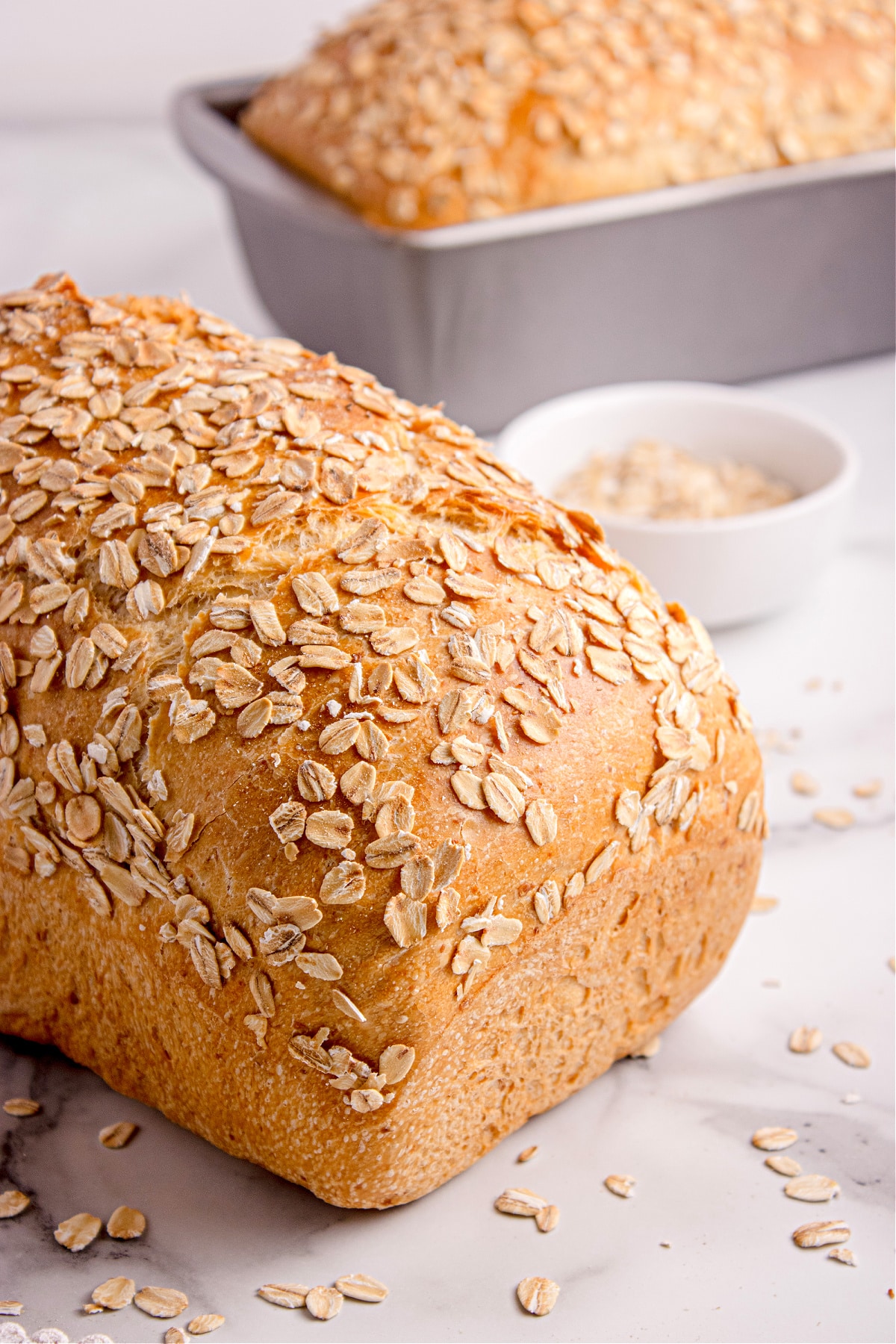 soft honey oat bread loaves Two loaves of soft honey oat bread topped with oats cooling beside a small bowl of oats.