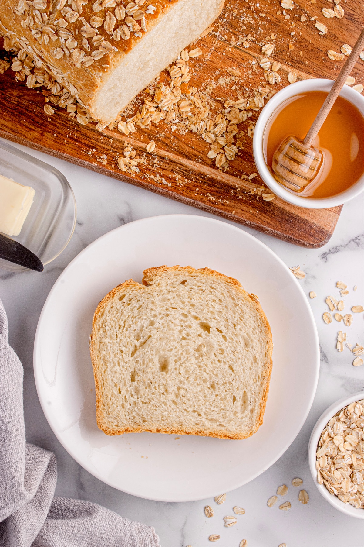 slice of honey oatmeal bread Slice of honey oatmeal bread on a plate with butter and honey nearby.