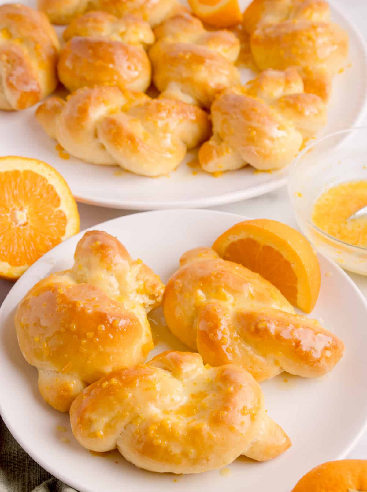 Orange knot rolls on a white plate, brushed with orange glaze and surrounded by orange slices.