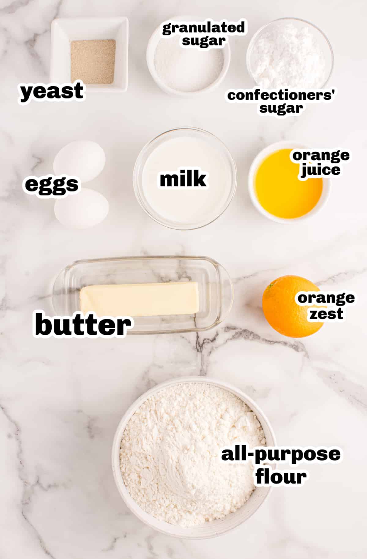 Overhead view of ingredients for orange rolls including flour, eggs, butter, milk, orange juice, and zest.