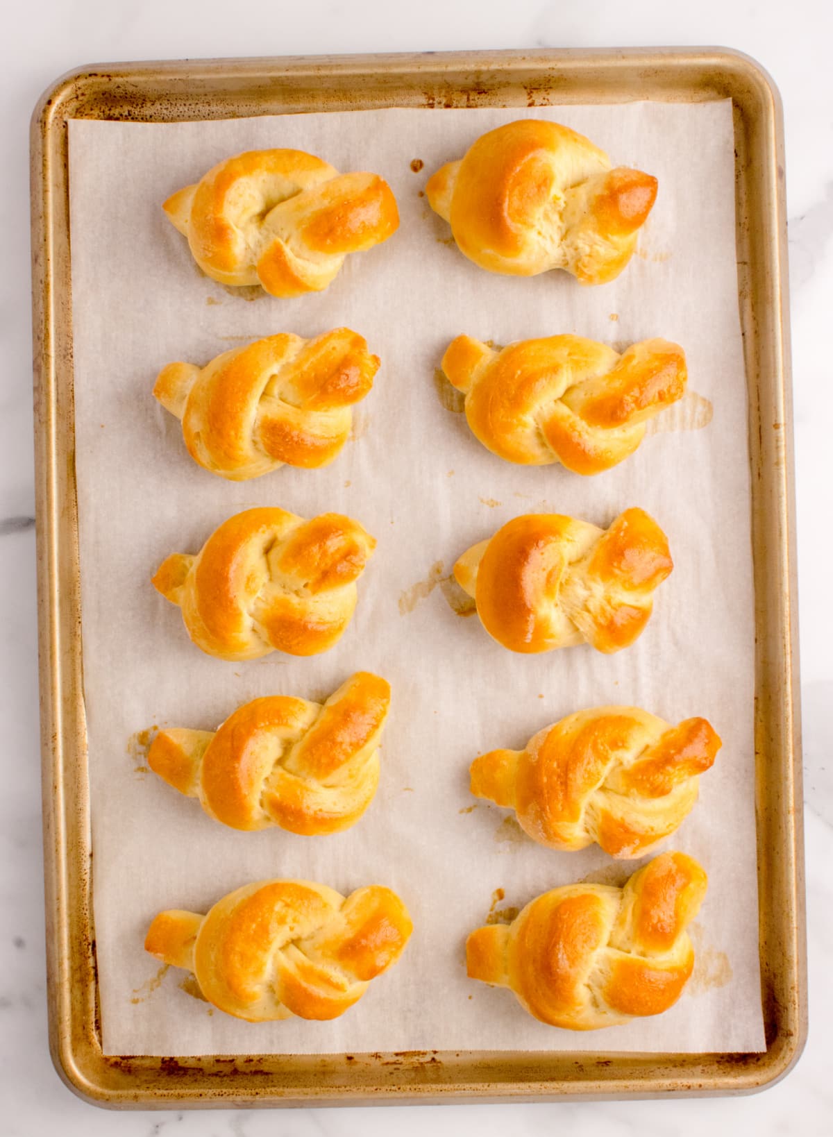 Freshly baked orange bread knots cooling on a parchment-lined baking sheet.