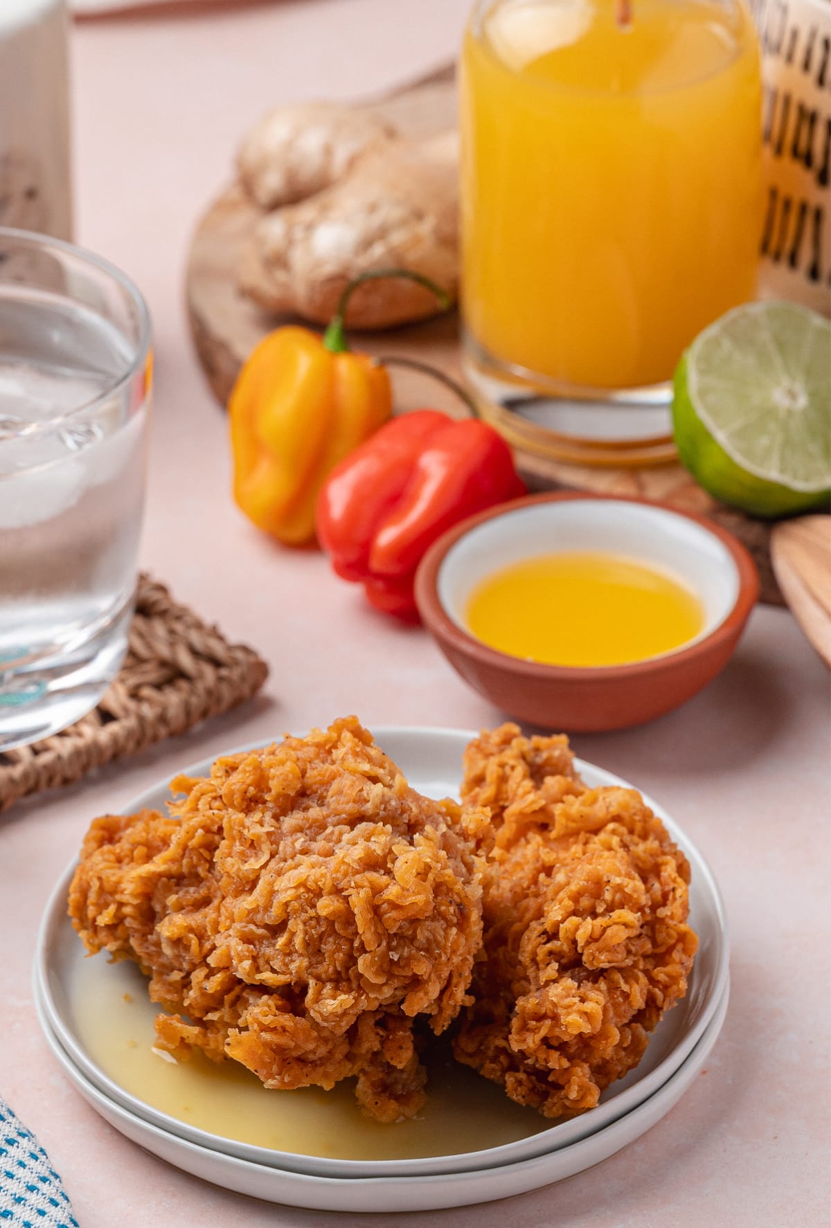 Fried chicken served with a drizzle of homemade pineapple habanero hot sauce, surrounded by fresh ginger, limes, and peppers.