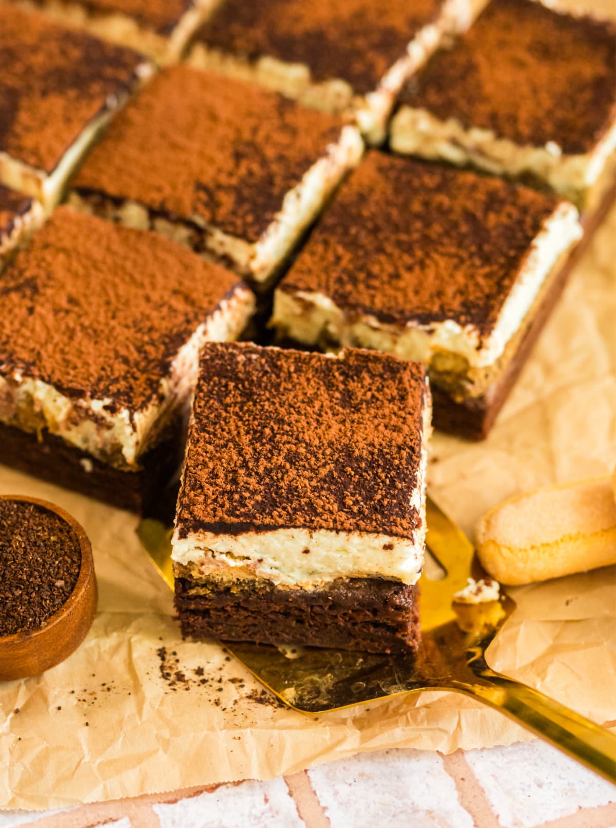tiramisu brownies cut into squares topped with cocoa powder, served on parchment paper.