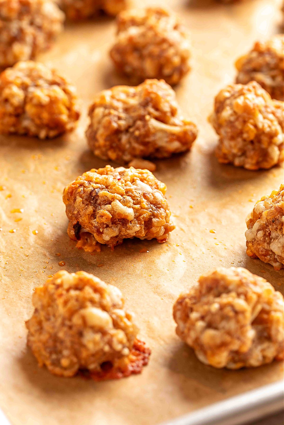 Baked sausage balls resting on a parchment-lined sheet pan. Freshly baked sausage balls cooling on a parchment-lined sheet pan, showing their crisp golden edges and melted smoked cheddar pockets.