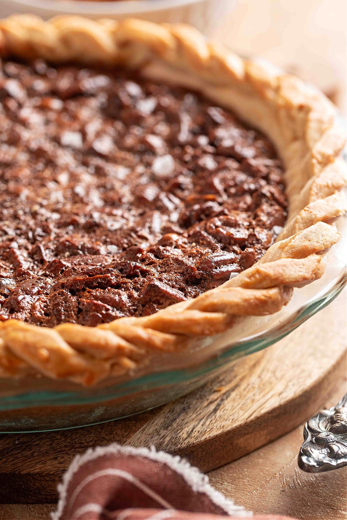 Close-up of a chocolate hazelnut pecan pie with a golden braided crust and a glossy Nutella-filled surface sprinkled with flaky sea salt.