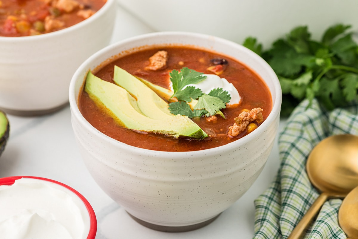 A bowl of ground chicken chili topped with sliced avocado, sour cream, and cilantro for Noble Pig.