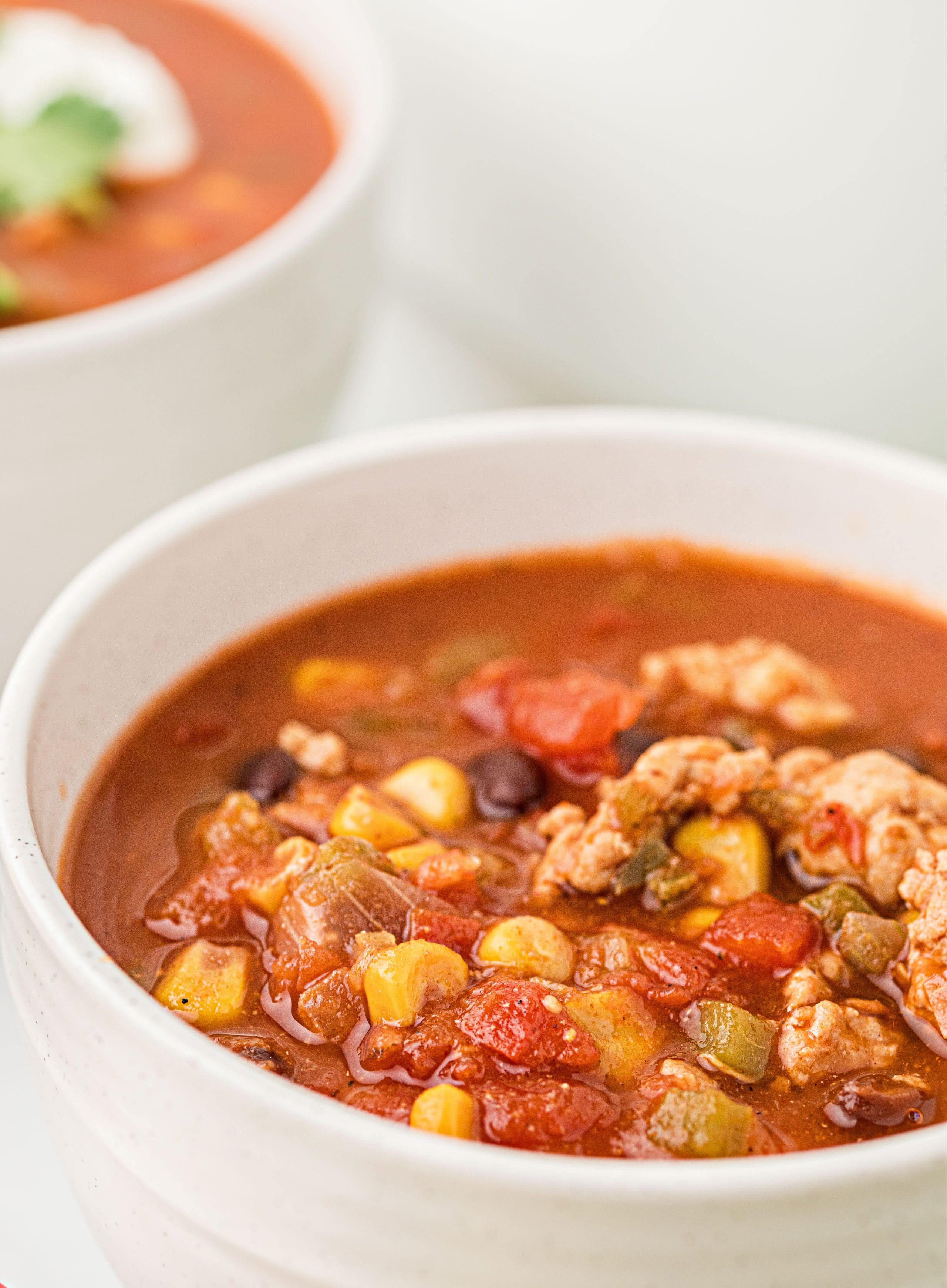 Close-up of a bowl of chili showing chunks of chicken, black beans, corn, and tomatoes in a rich red sauce.
