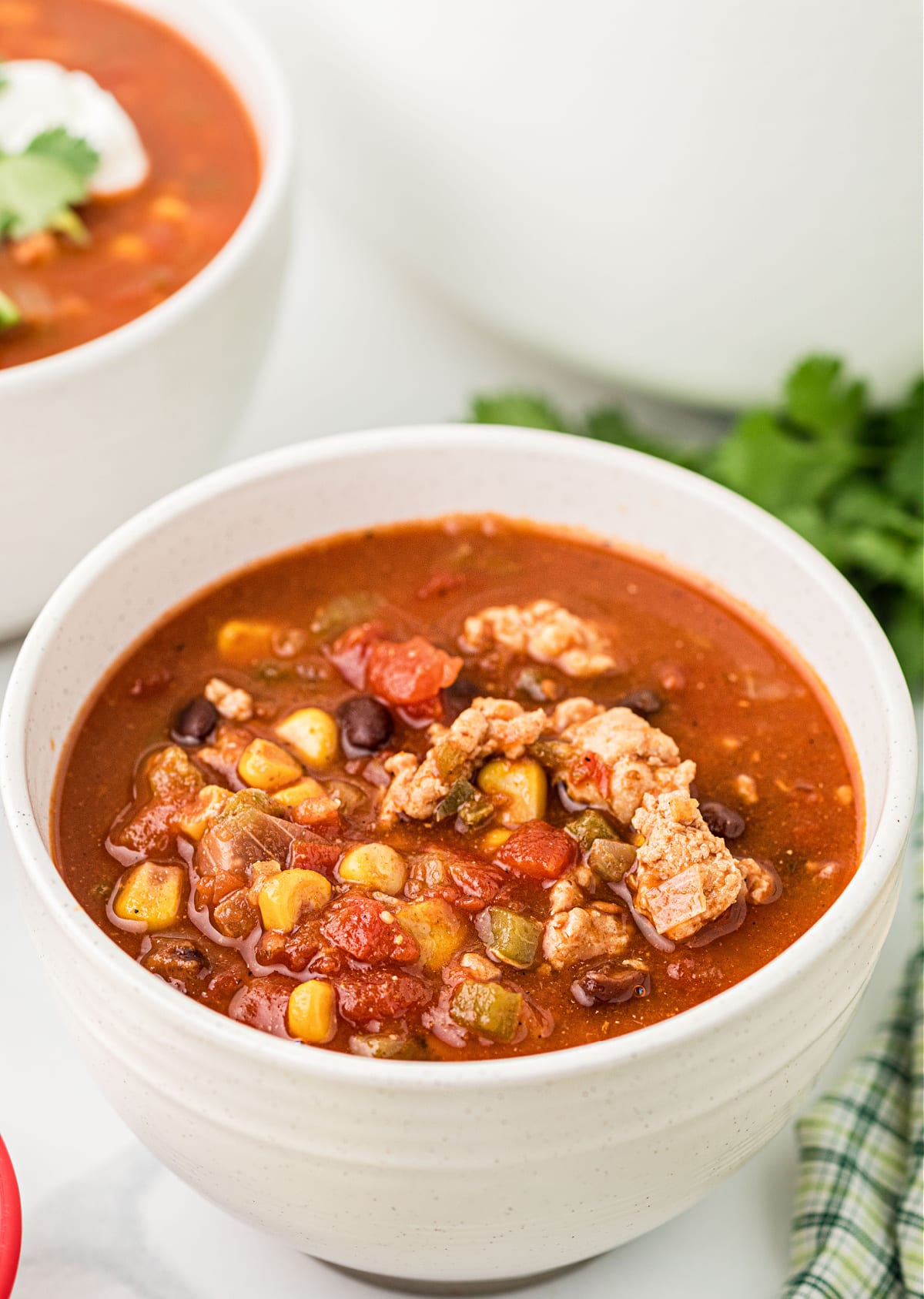 A white bowl filled with hearty chili made with chicken, corn, black beans, and diced tomatoes.