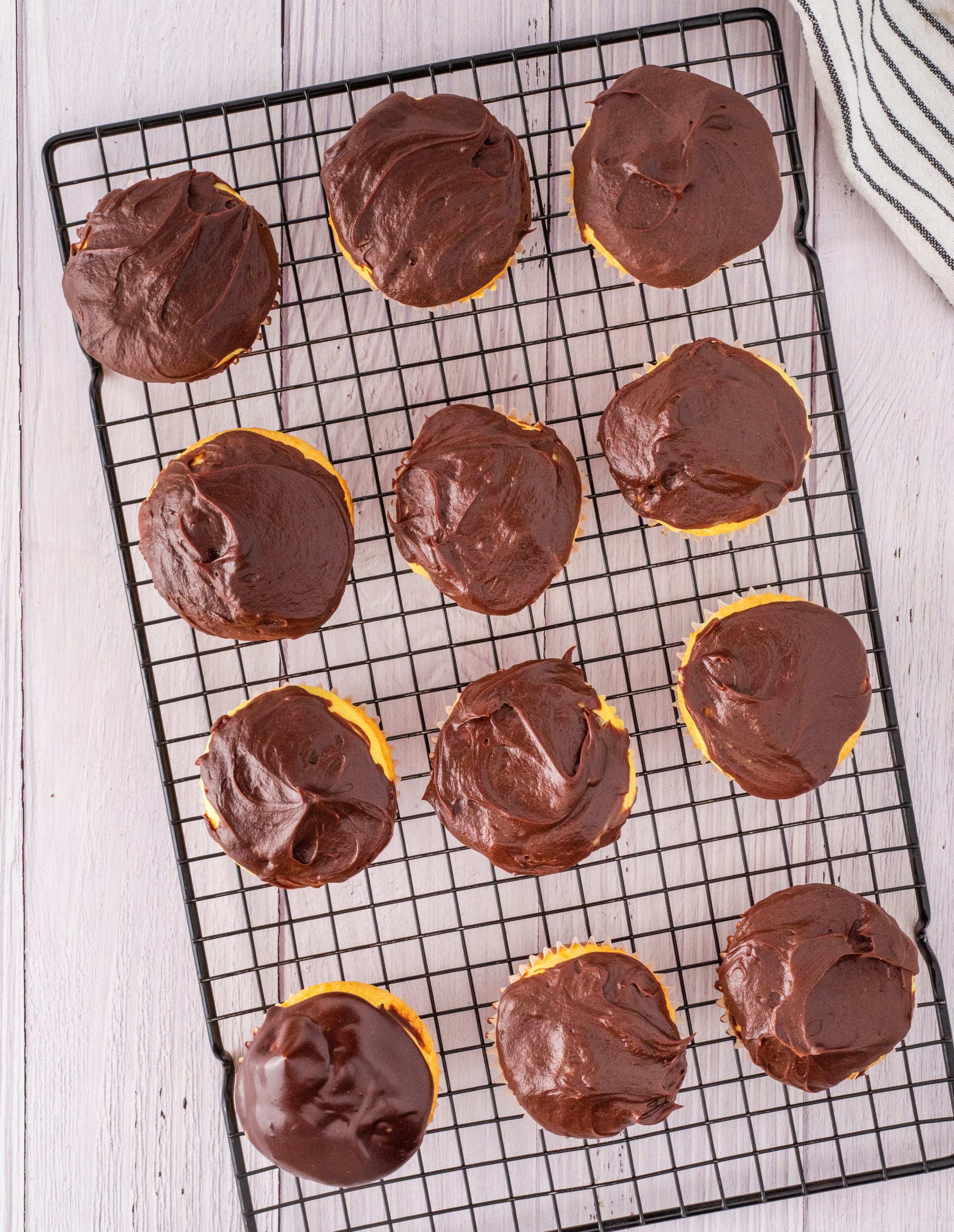 Cupcakes with Chocolate Ganache on Cooling Rack Freshly frosted cupcakes with chocolate ganache cooling on a wire rack, showing the thick glossy layer set over vanilla cream centers