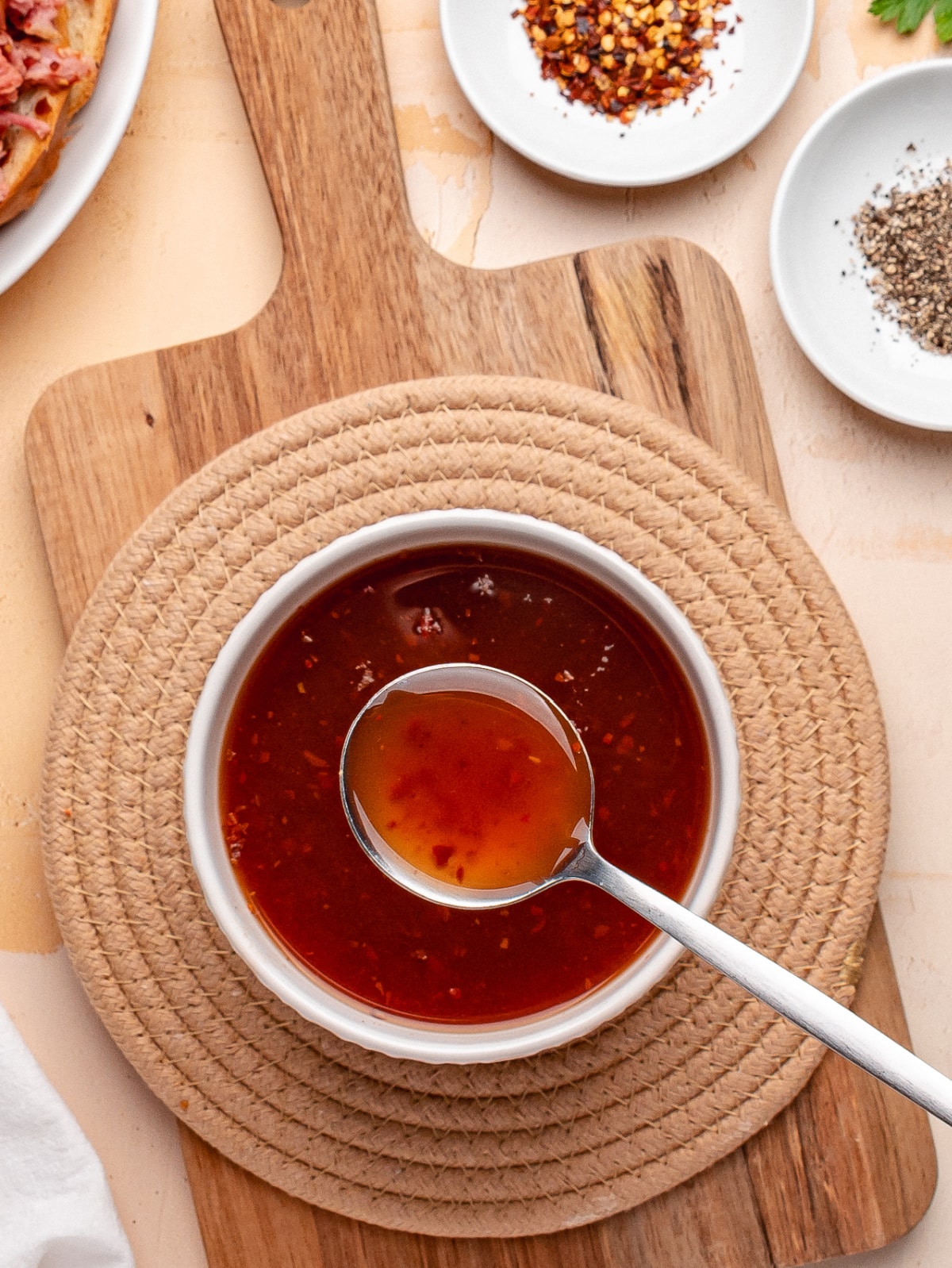 Western Carolina BBQ sauce in bowl with ladle. Bowl of Western Carolina vinegar BBQ sauce with ladle on wooden board surrounded by spices.