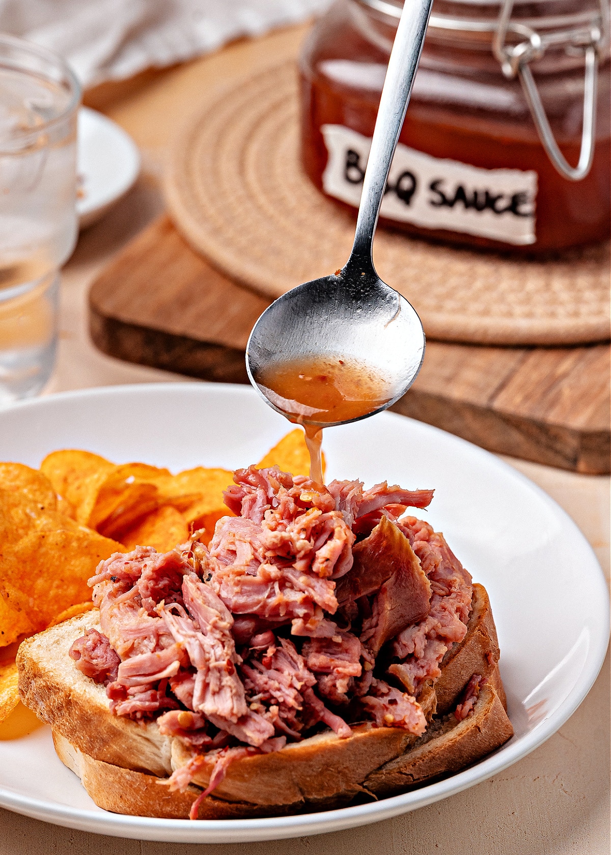 Western Carolina BBQ sauce poured over pulled pork sandwich. Ladle pouring Western Carolina vinegar BBQ sauce over pulled pork sandwich on white bread, for Noble Pig.