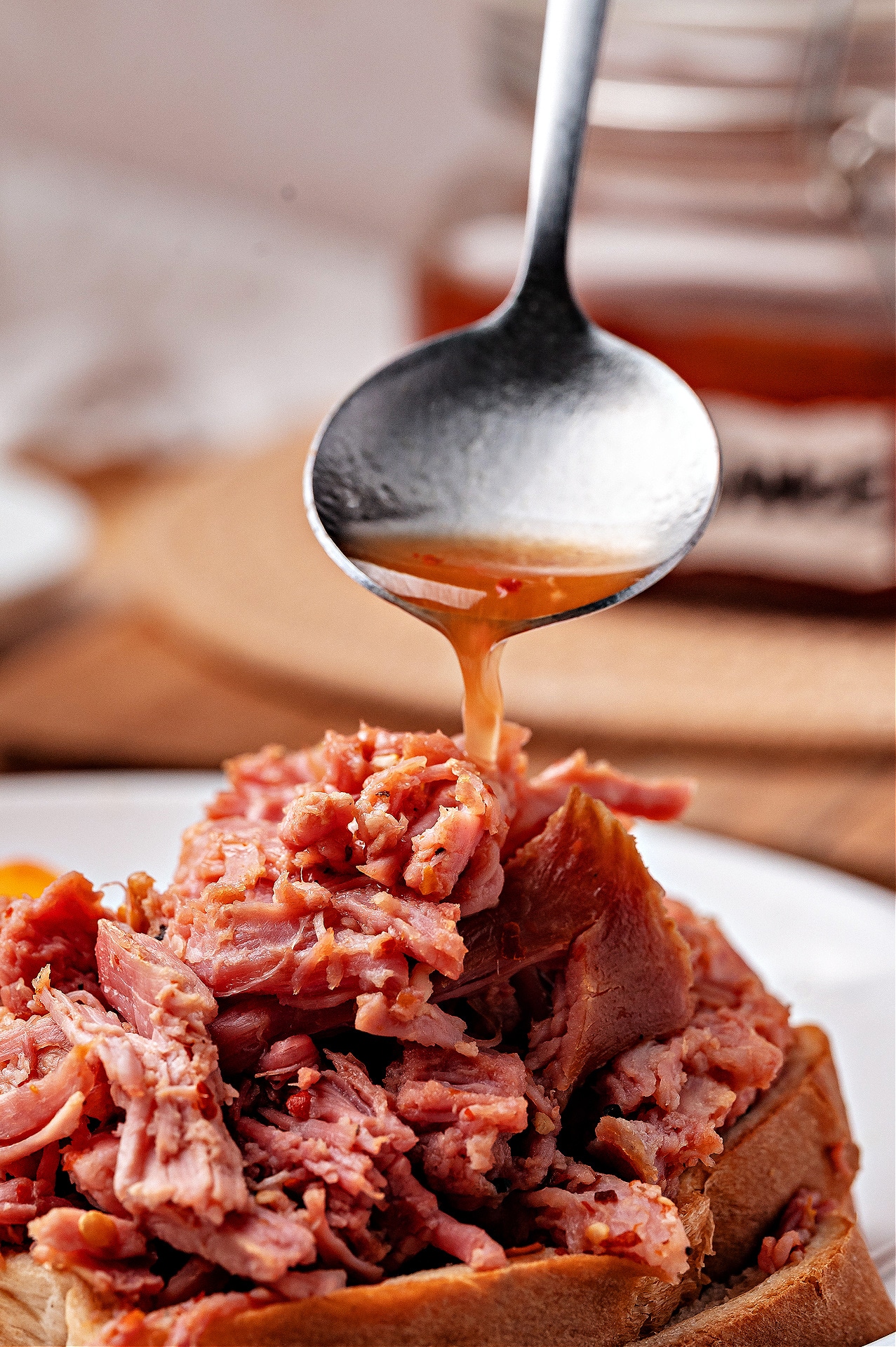 Tangy Western Carolina barbecue sauce poured over smoked pulled pork. Spoon pouring tangy Western Carolina barbecue sauce over shredded smoked pork sandwich.