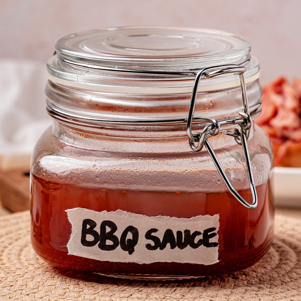 Jar of Western Carolina BBQ sauce labeled BBQ Sauce on a woven mat with pulled pork in the background.