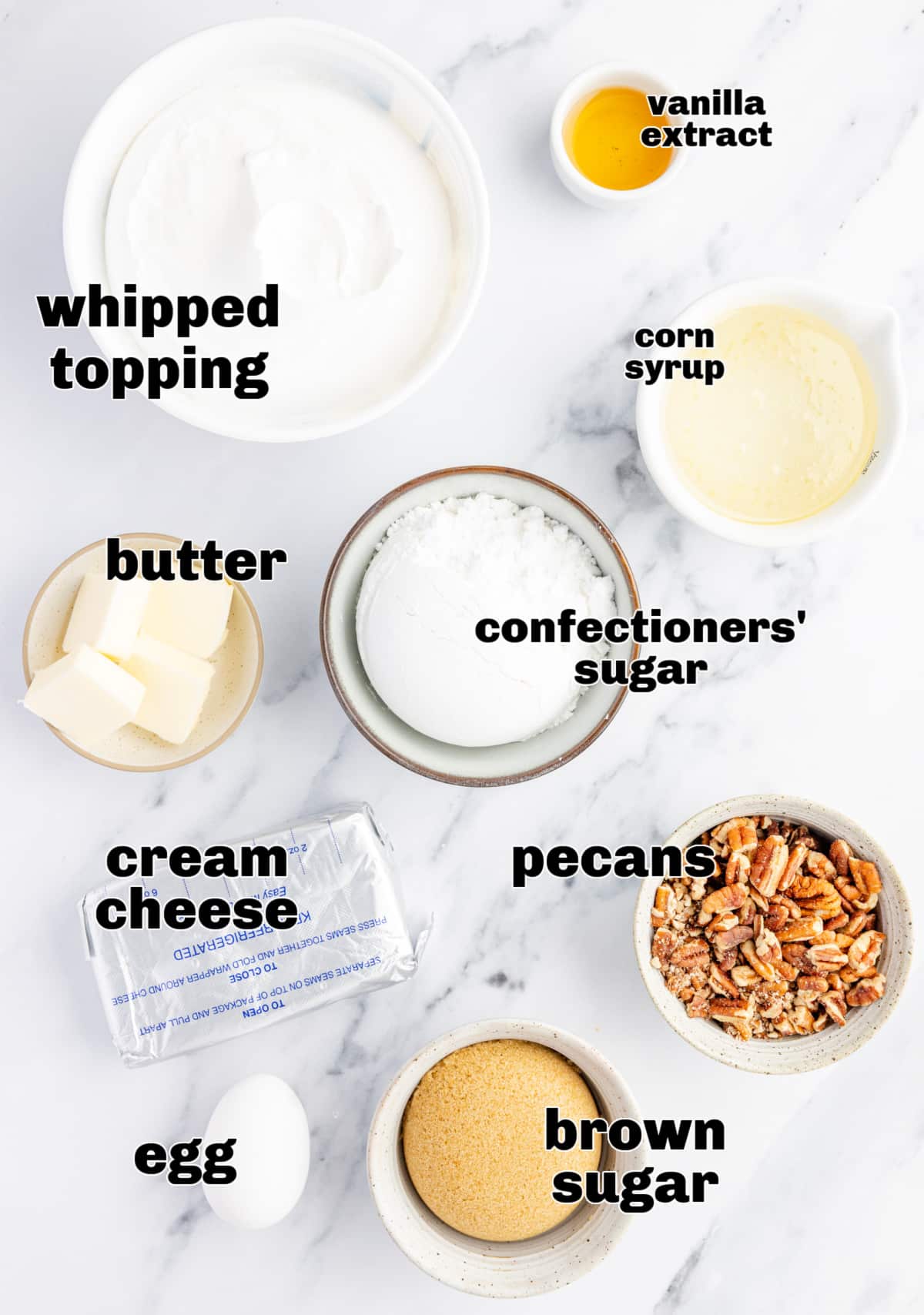 Ingredients for the cream cheese and caramel pecan dip Ingredients for a cream cheese dessert dip arranged on a marble surface, including whipped topping, brown sugar, pecans, confectioners’ sugar, butter, corn syrup, vanilla extract, and an egg.
