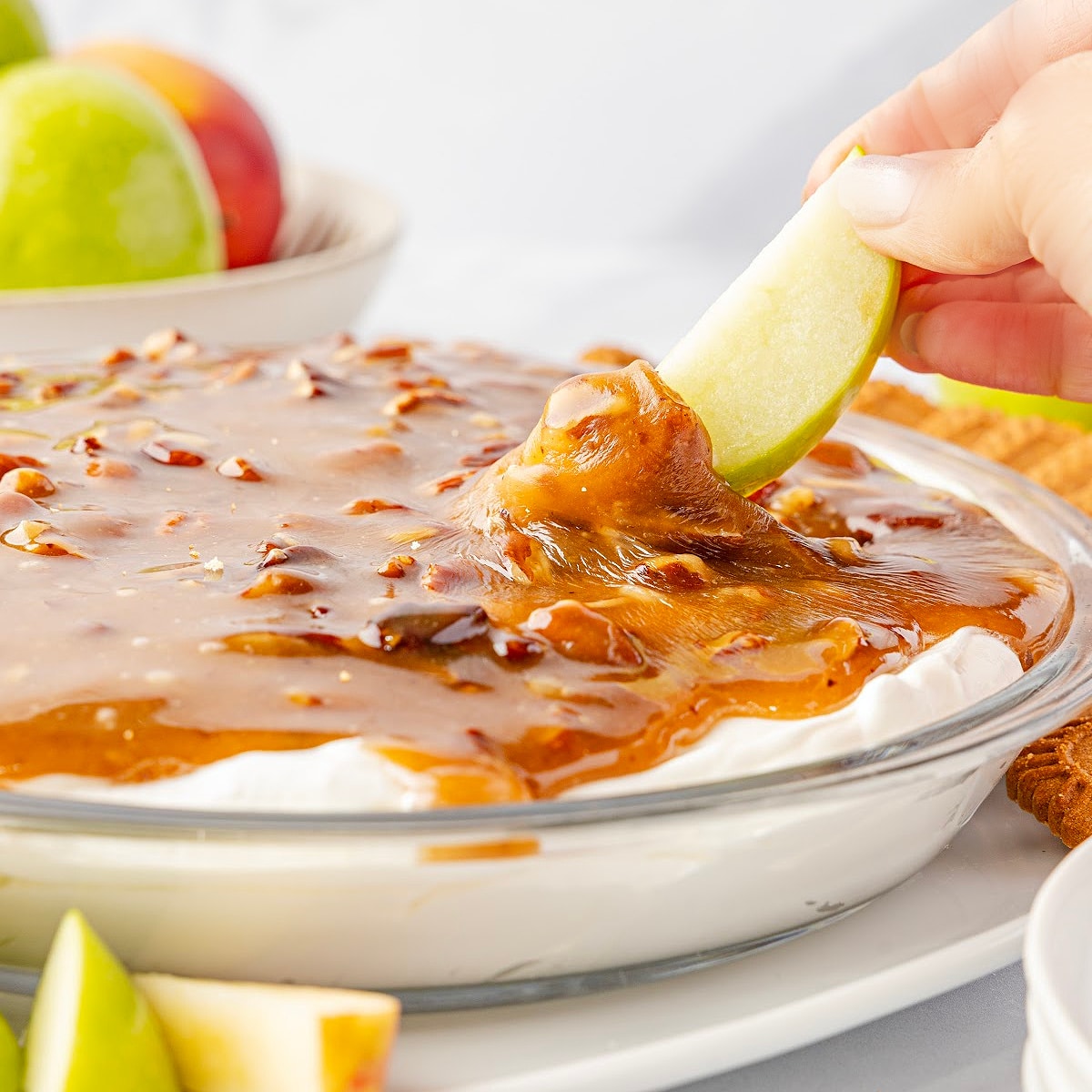 Pecan pie dip with caramelized brown sugar pecan topping and a crisp apple slice dipped in the creamy layer by Noble Pig.