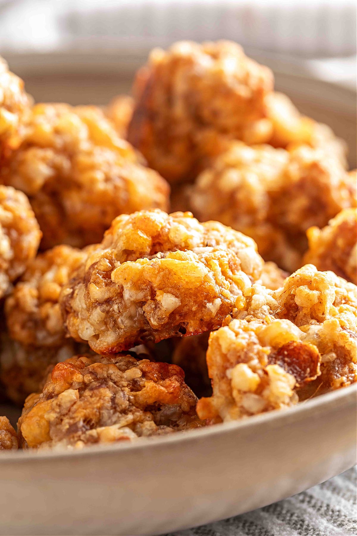 A bowl filled with freshly baked sausage balls. A close-up view of baked sausage balls piled in a shallow bowl, showing their crisp edges, melted smoked cheddar, and golden-brown surface.