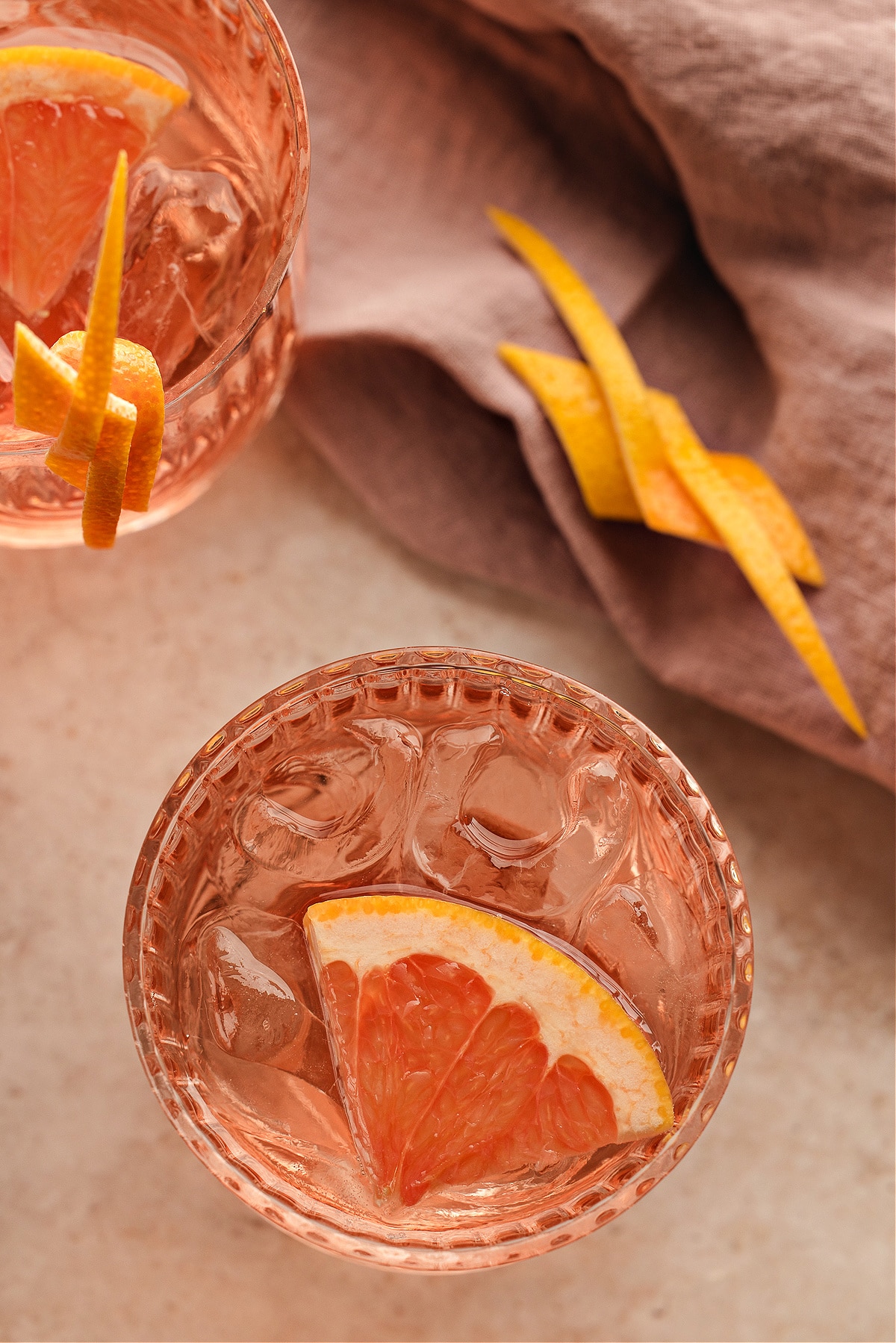 Two pale pink Lillet Rosé spritz cocktails viewed from above, each served over ice with fresh grapefruit and long citrus twists, set beside a soft mauve linen.