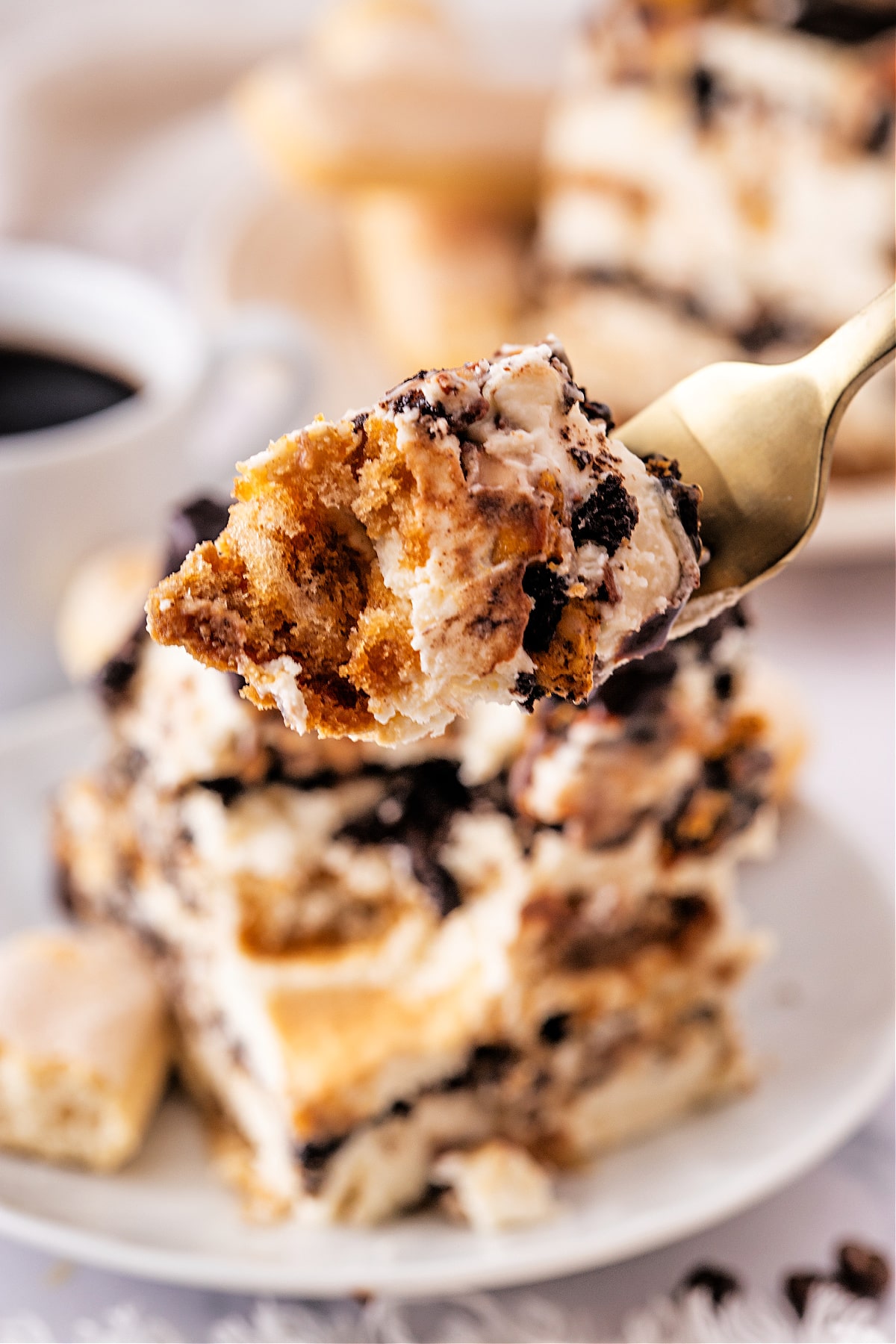 Forkful of tiramisu showing espresso-soaked layers, mascarpone caramel cream, and crushed cookies in each bite.