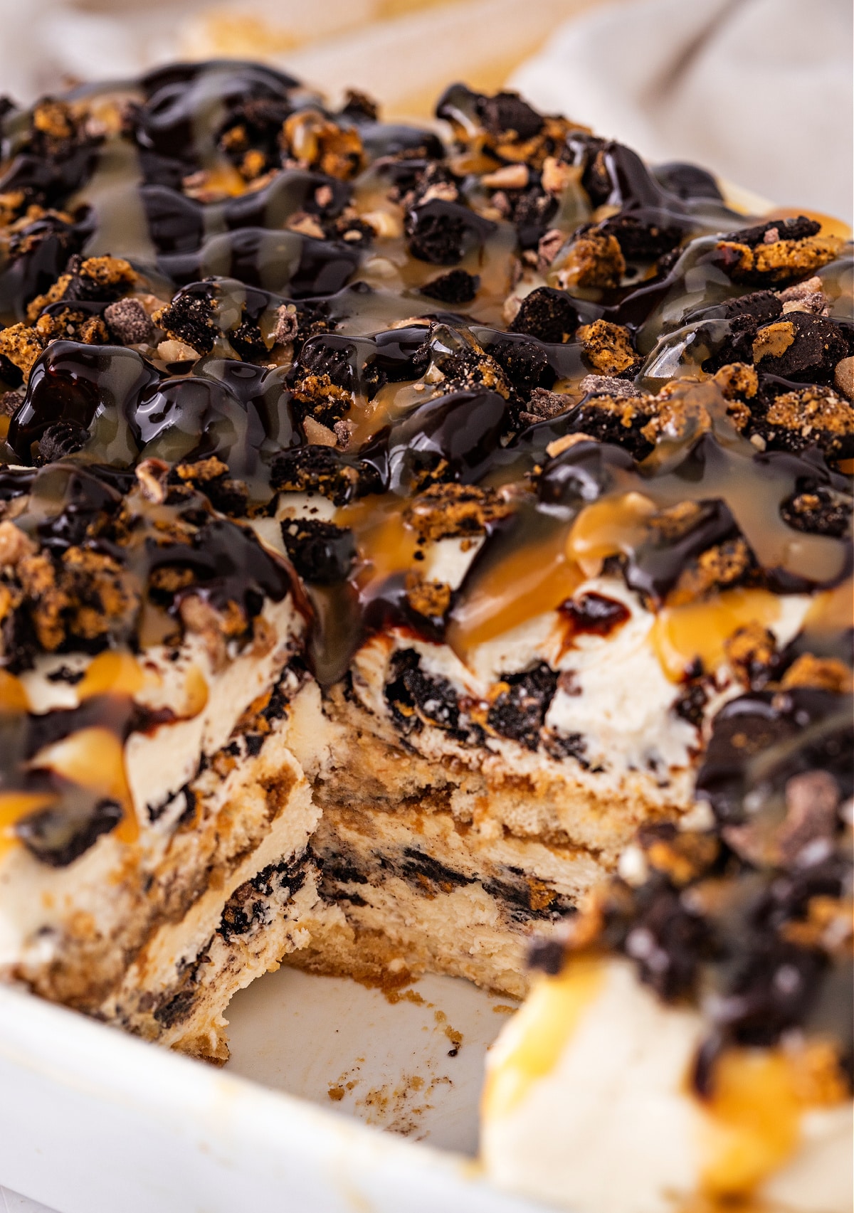 Close-up of tiramisu layers with espresso-soaked ladyfingers, mascarpone caramel cream, crushed cookies, and drizzled chocolate and caramel.