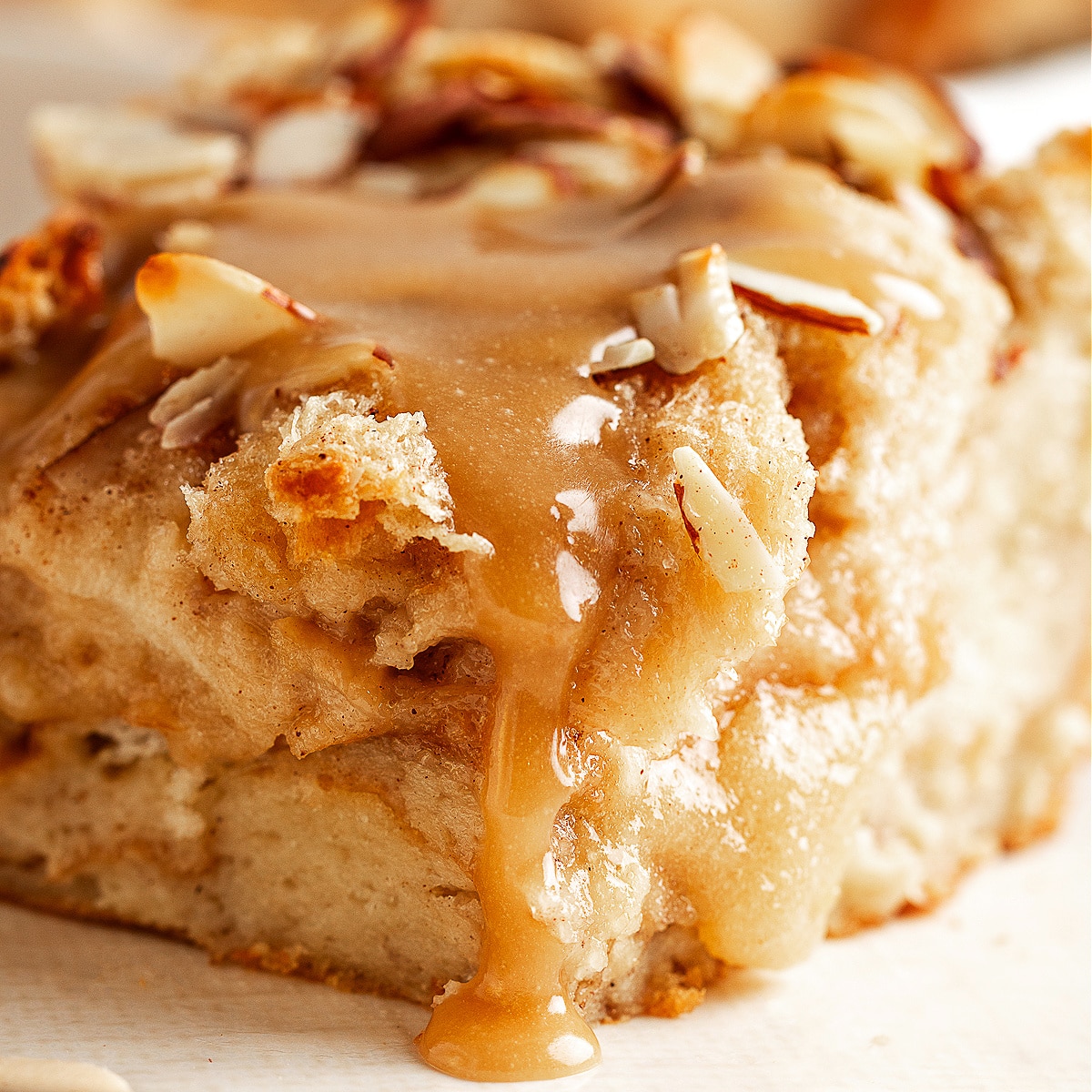 A slice of almond cream bread pudding with brown sugar glaze dripping down the sides, showing its soft, custardy center.