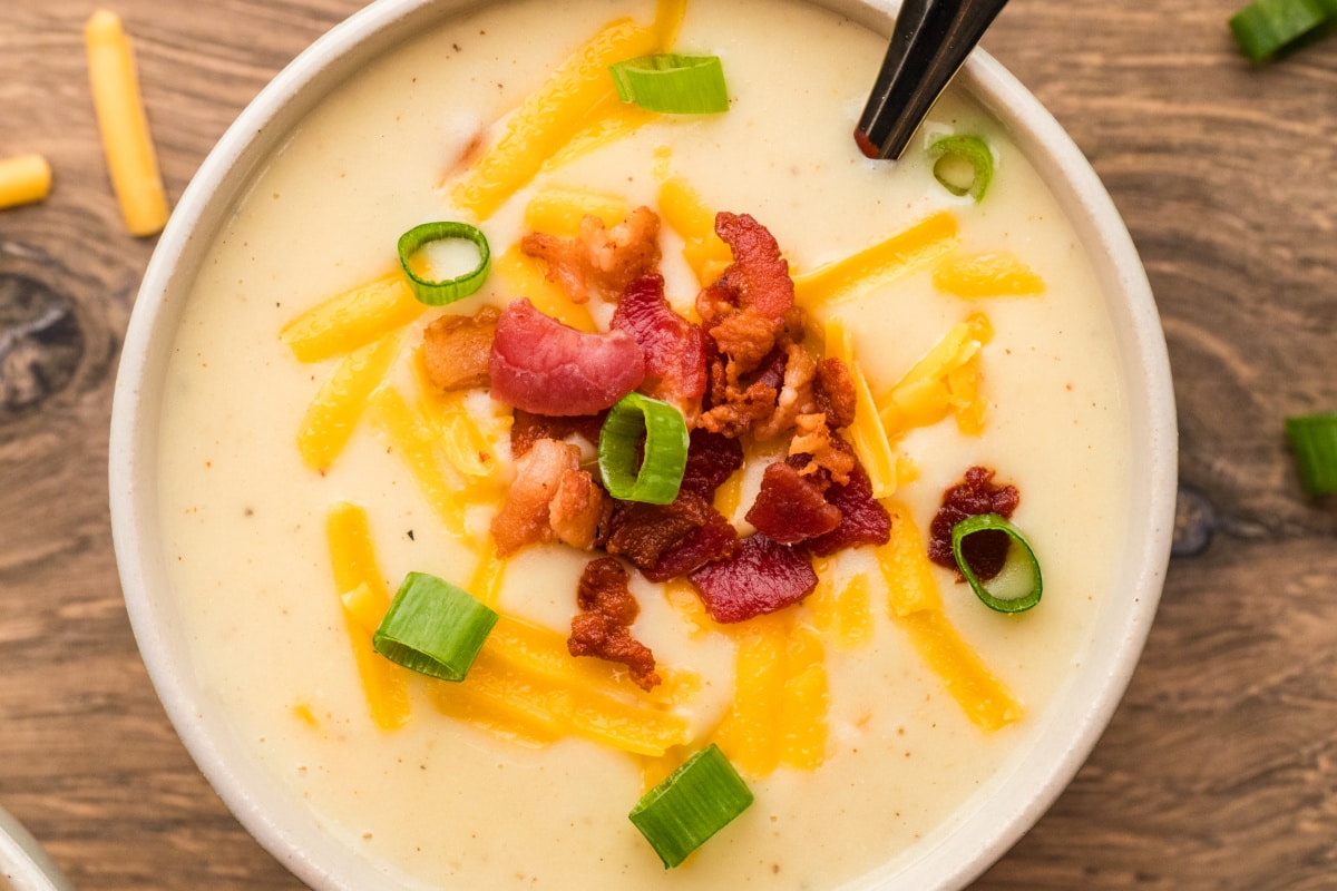 Creamy baked potato soup finished with bacon, cheddar, and scallions in the bowl. A bowl of creamy baked potato soup topped with crisp bacon, shredded cheddar, and sliced scallions.