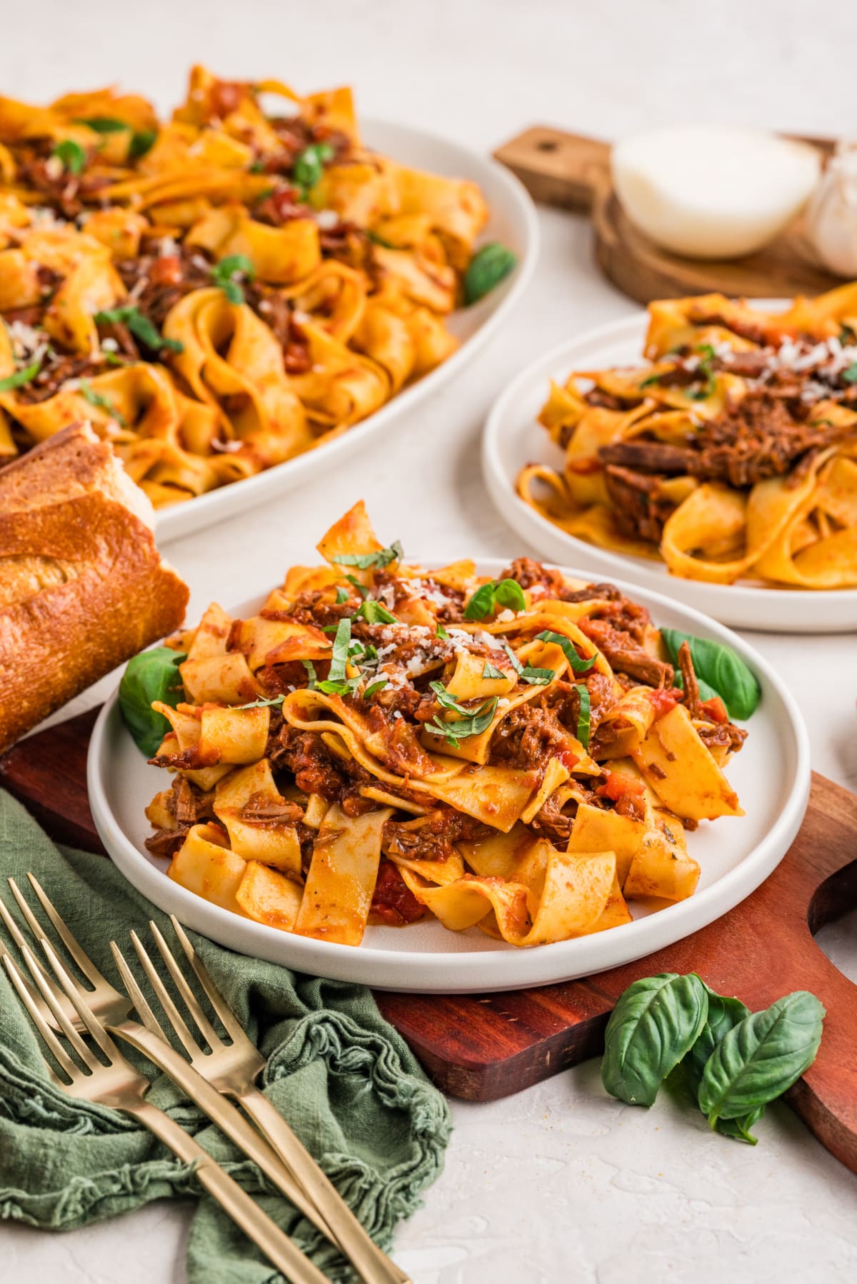 Plates of pappardelle tossed with tender shredded beef ragù, served with fresh basil and crusty bread, ready at the table.