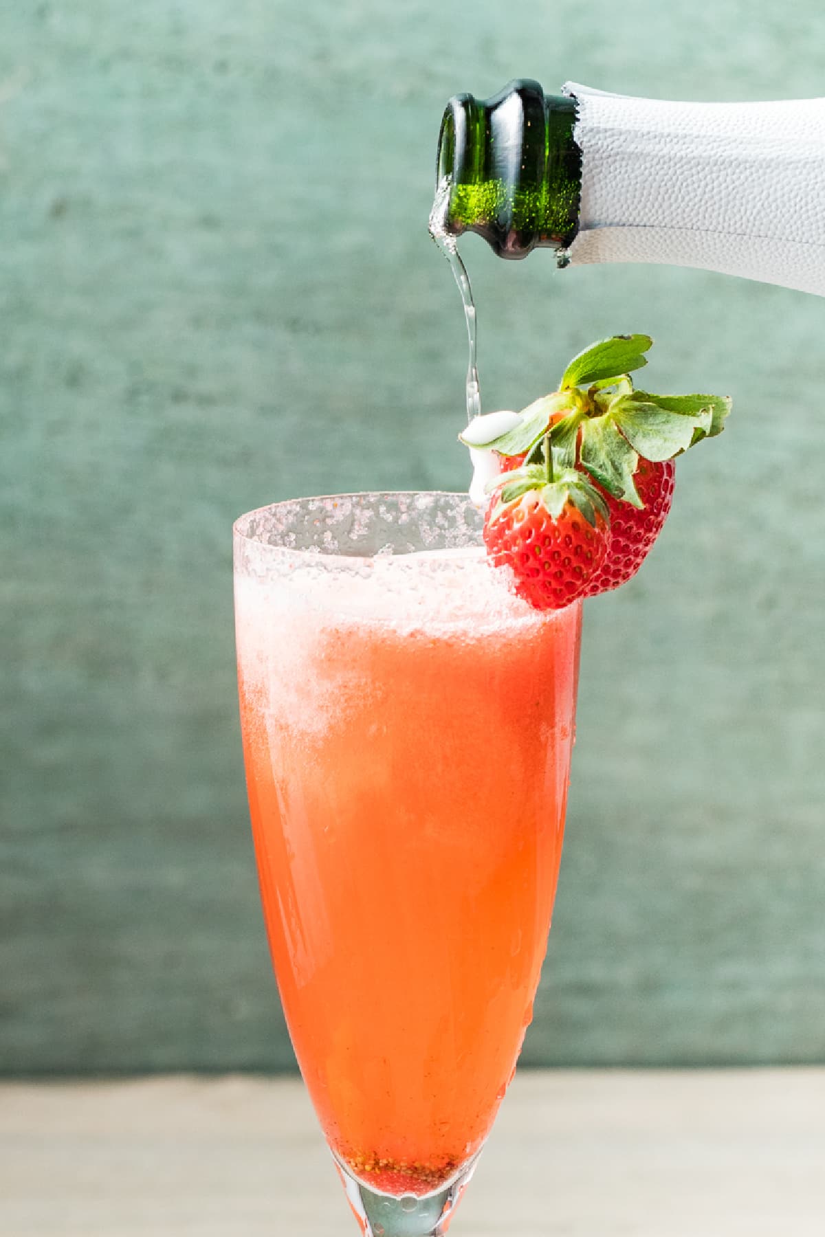 Sparkling wine being poured into a champagne flute filled with strawberry purée.