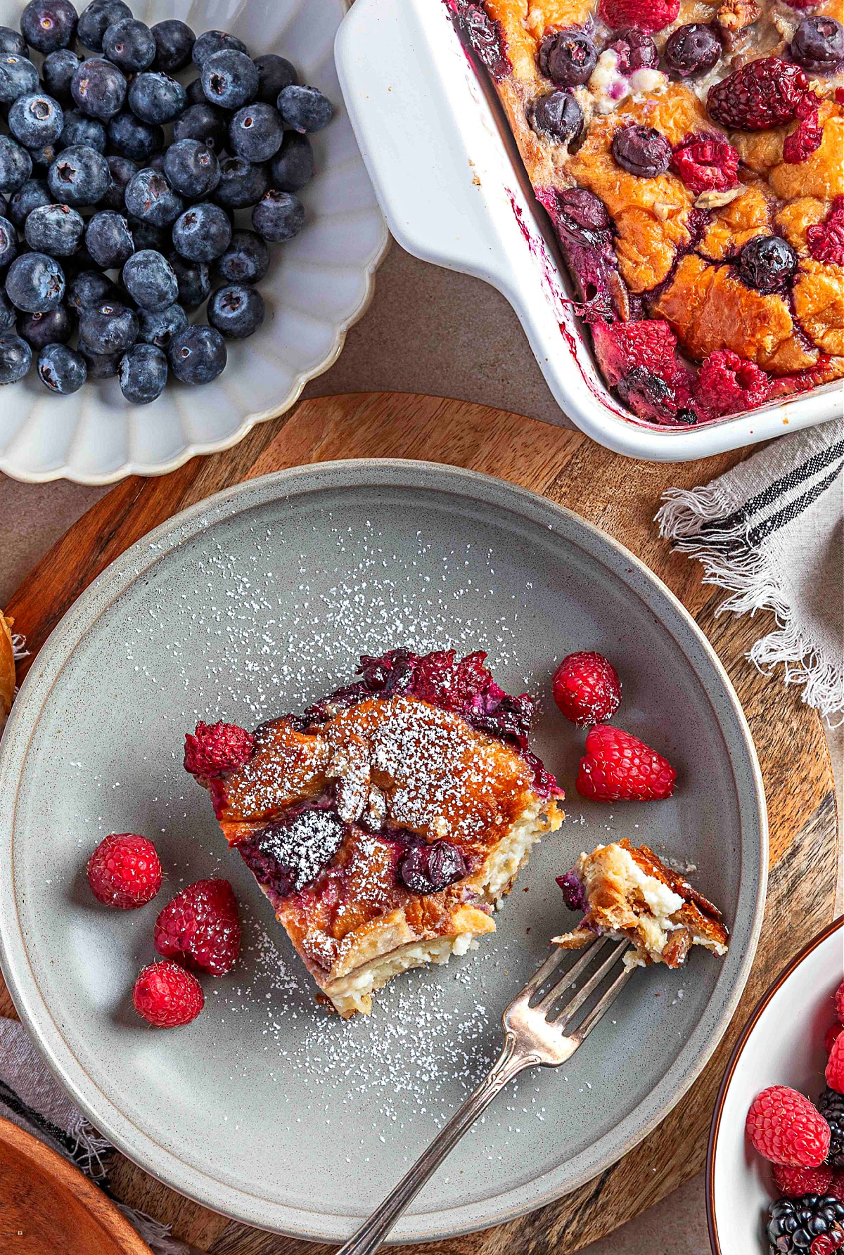 Berry croissant french toast casserole served on a plate with a custardy center, baked berries, and a light dusting of confectioners’ sugar.