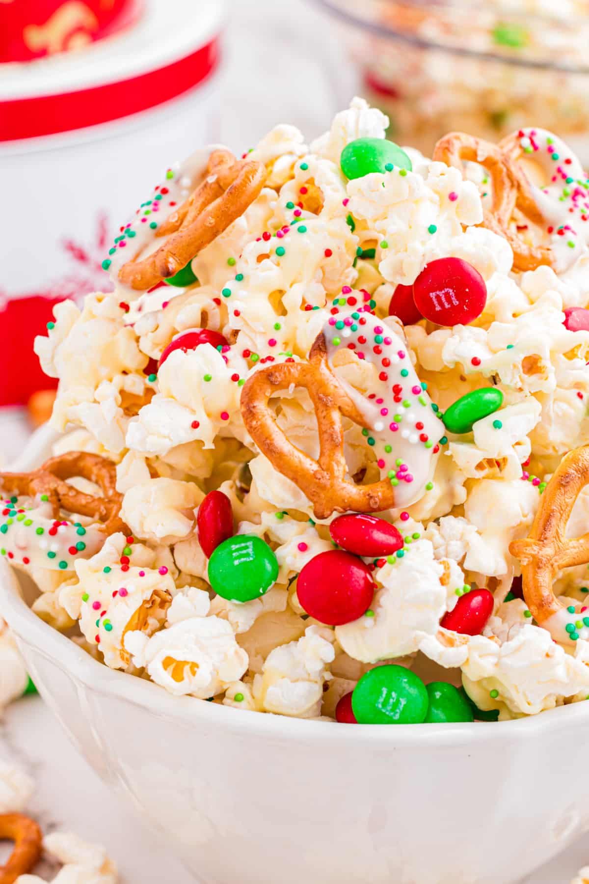 A close-up shows the texture of Christmas popcorn mix with pretzels and candy. Close-up of Christmas popcorn mix with white chocolate–coated popcorn, pretzels, holiday sprinkles, and candy-coated chocolates.